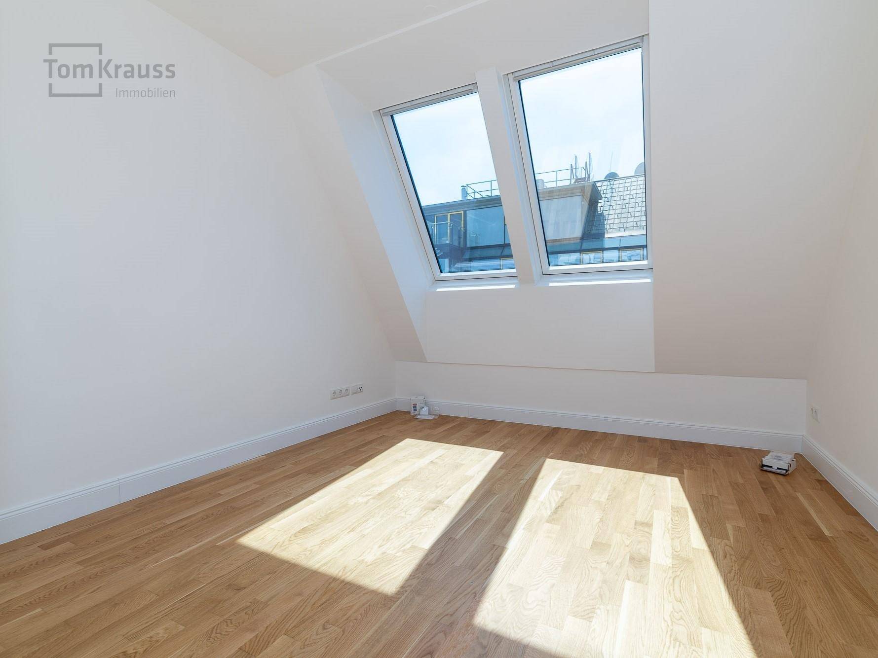 Helles, unmöbliertes Schlafzimmer mit Dachschrägen, Dachfenstern und Holzboden.