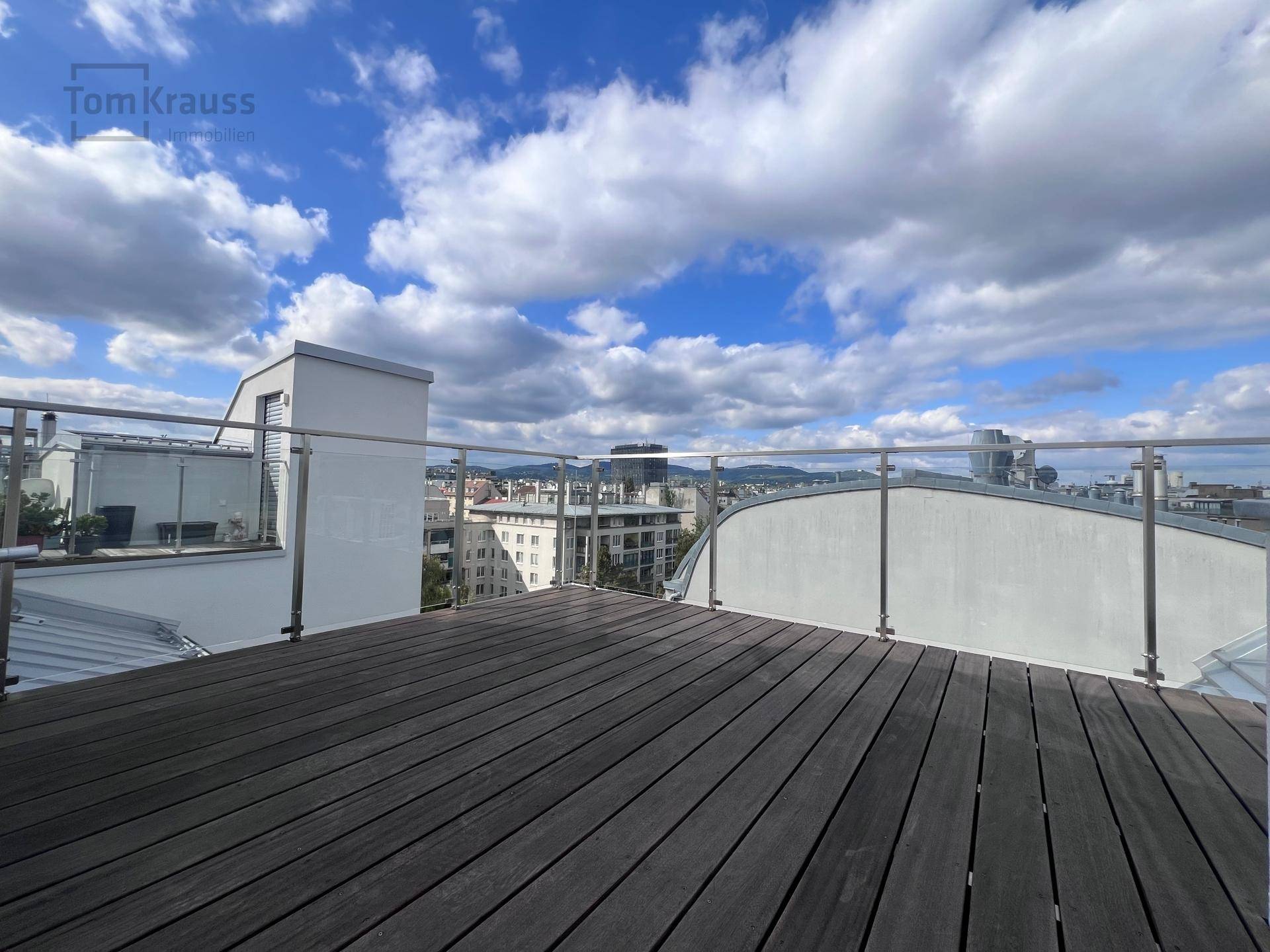 Weitläufige Dachterrasse mit Holzboden und modernem Glasgeländer, ideal für Entspannung und Ausblick.