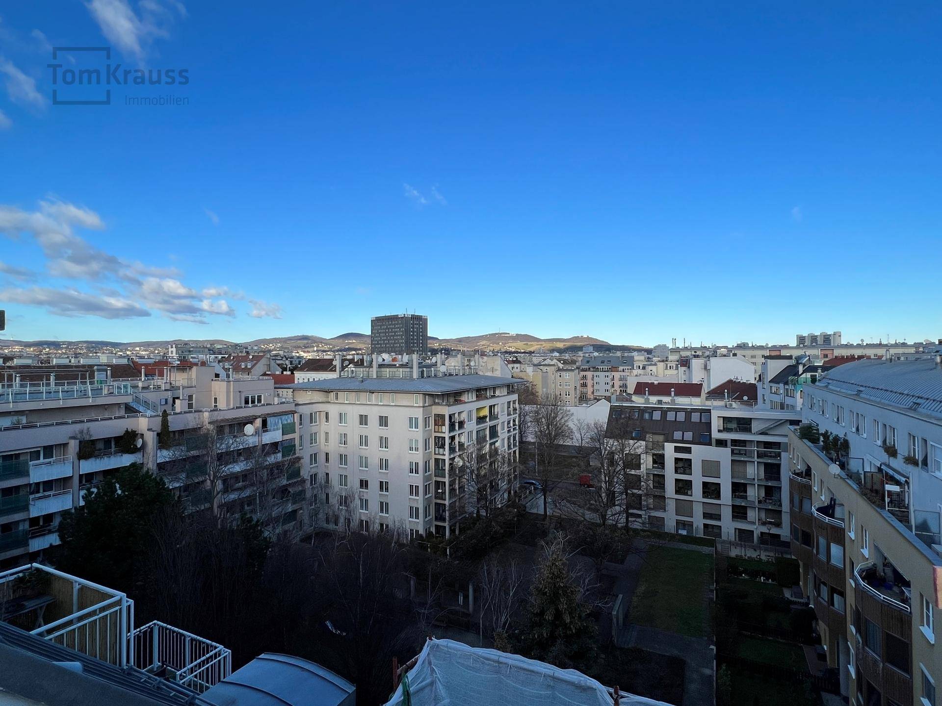 Panoramablick über die Stadt mit Wohngebäuden und Bergen am Horizont unter blauem Himmel.