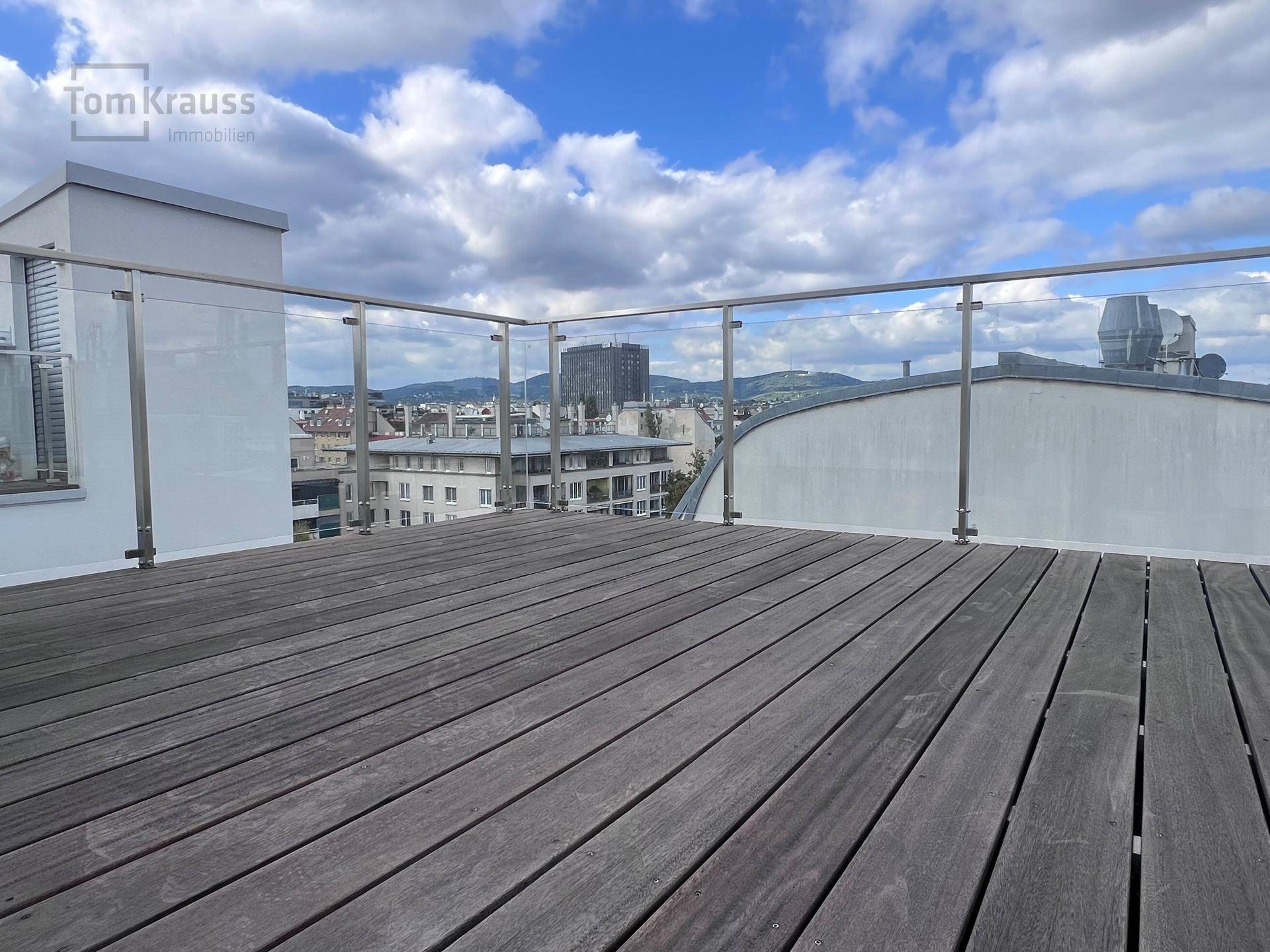 Leere Dachterrasse mit Holzboden und Glasgeländer, bietet einen weiten Blick über die Stadt.