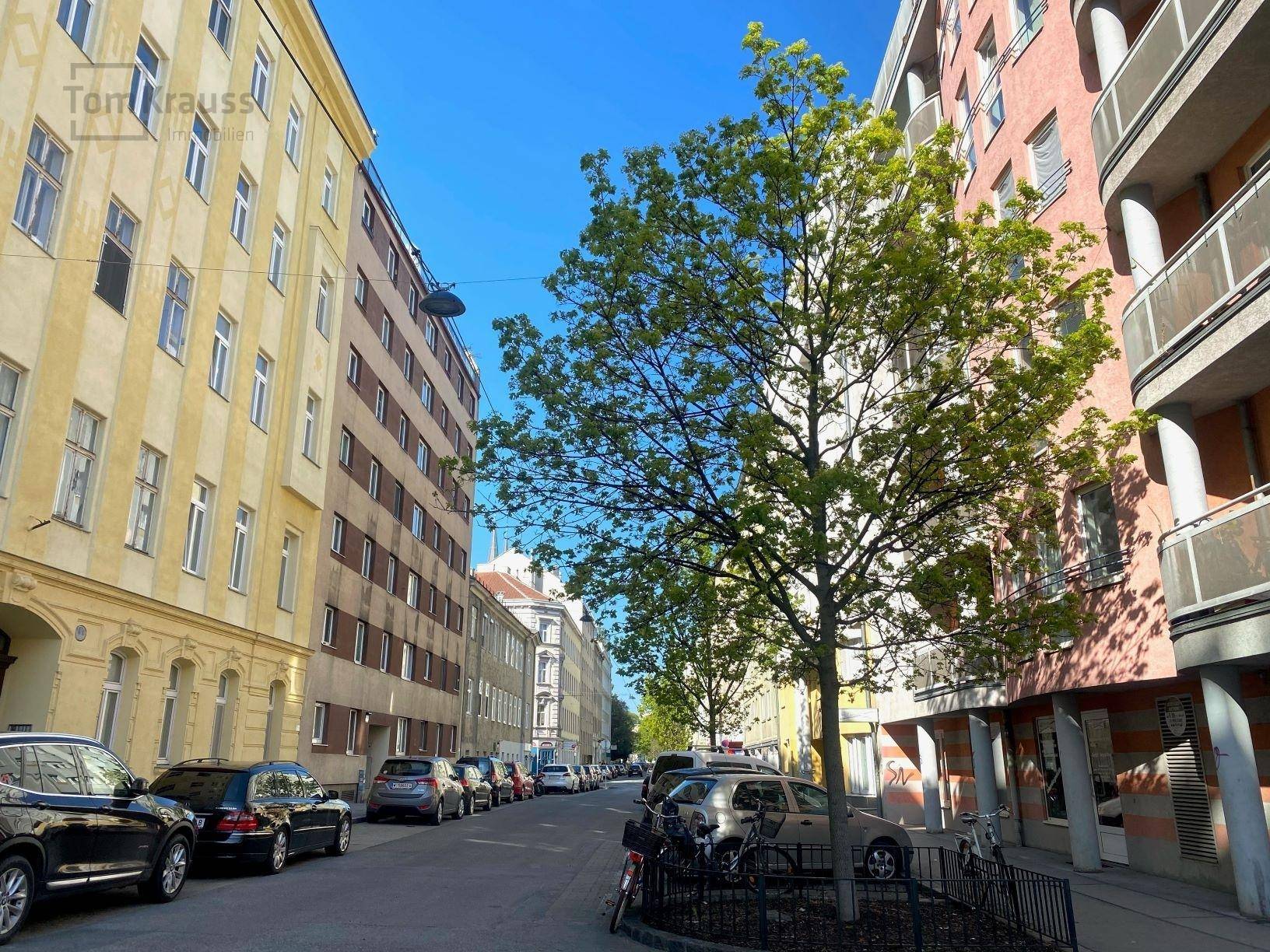 Ruhige Wohnstraße mit geparkten Autos und mehrstöckigen Gebäuden unter blauem Himmel.
