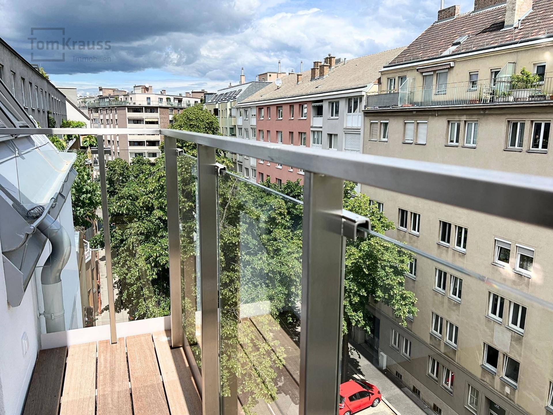 Geräumiger Balkon mit Holzboden und Glasgeländer, bietet einen weiten Blick über die städtische Umgebung.