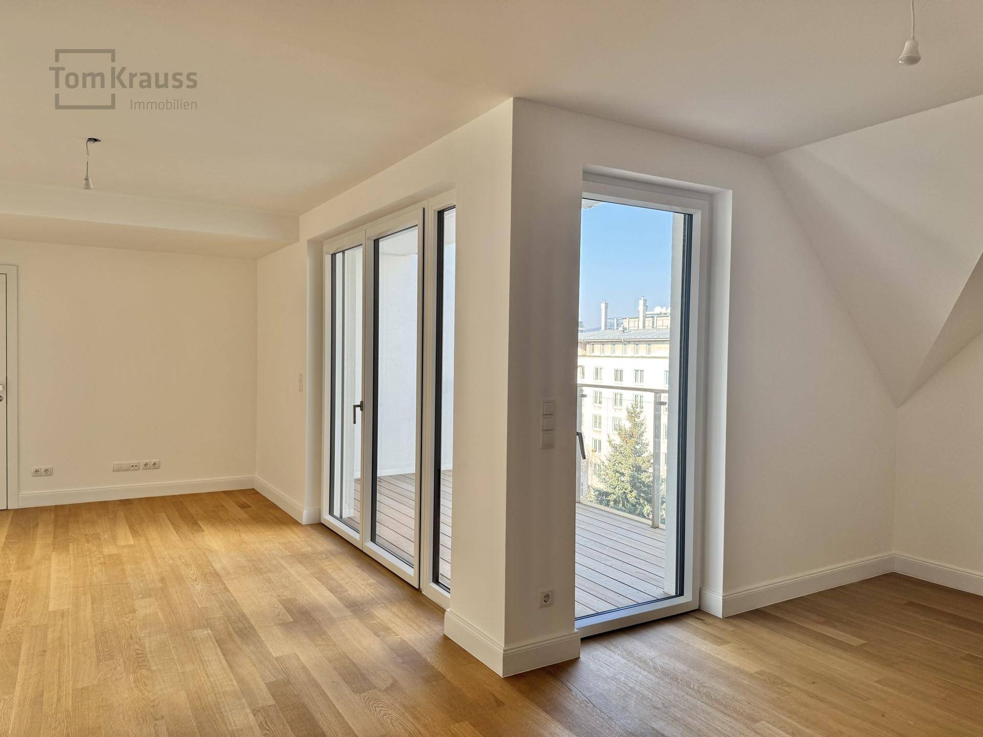 Heller Raum mit Holzboden, großen Schiebetüren zum Balkon und einer Dachschräge.