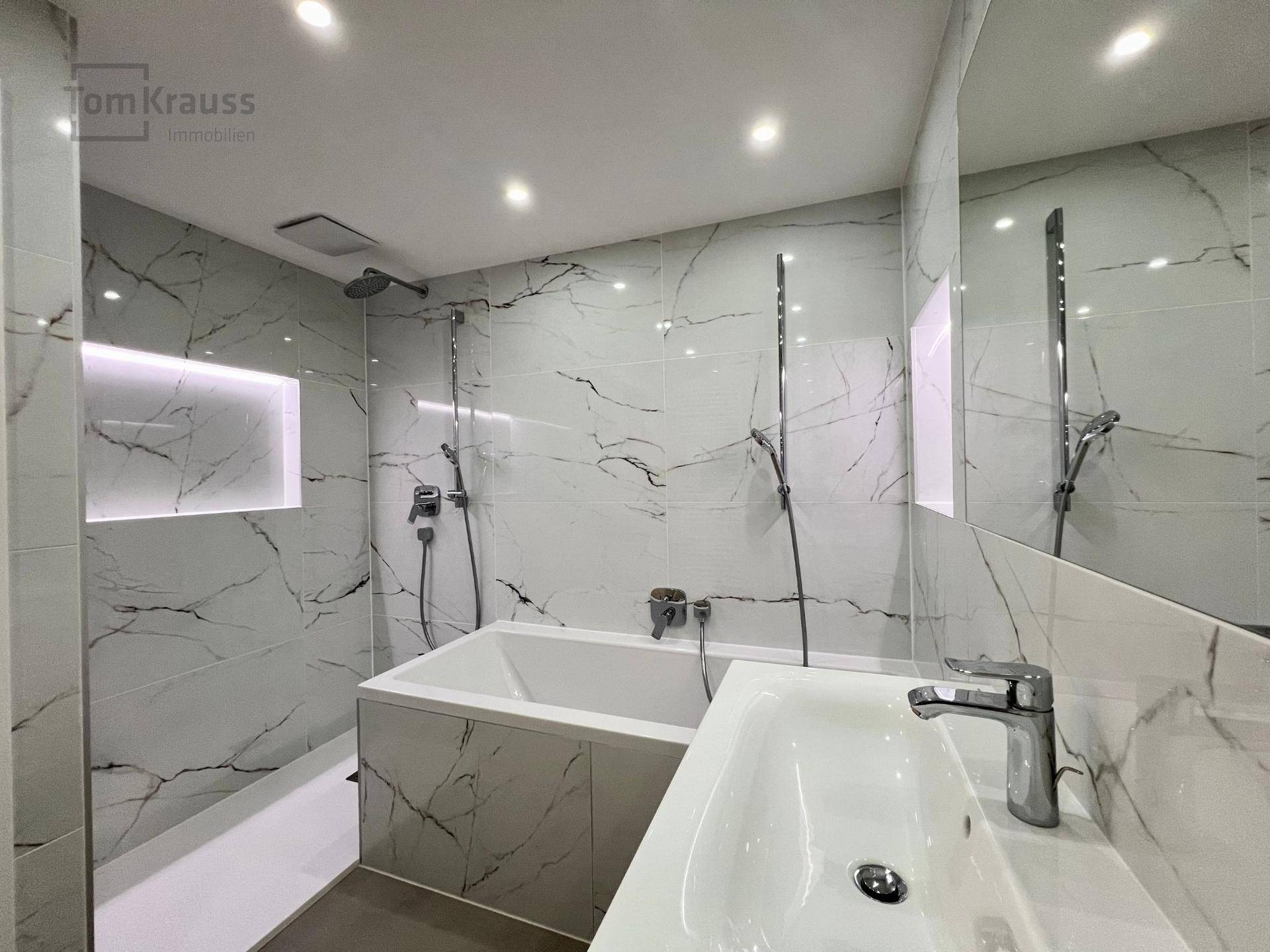Elegantes Badezimmer mit integrierter Badewanne, Dusche und großformatigen Fliesen in Marmoroptik.