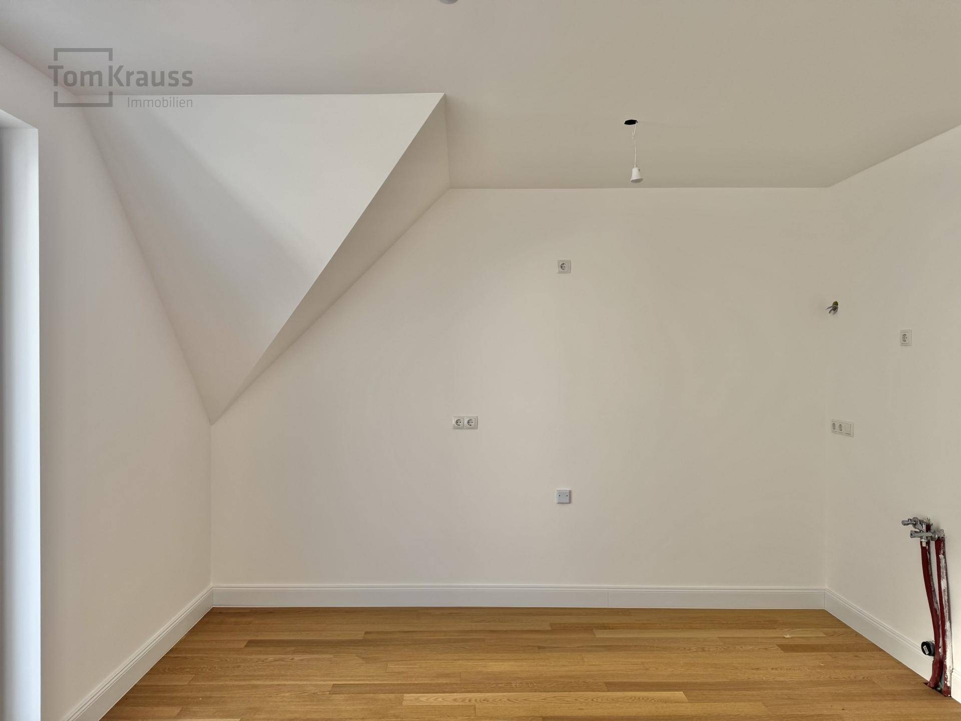 Leerer Raum mit Holzboden, weißen Wänden und einer markanten Dachschräge.