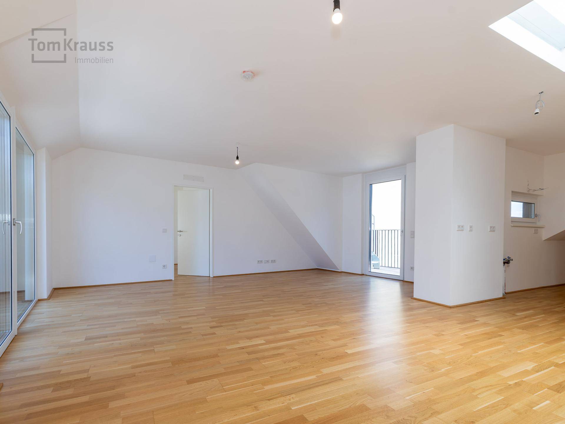 Geräumiger, leerer Wohn-Essbereich mit hellem Holzboden, großen Fenstern und Dachfenster.
