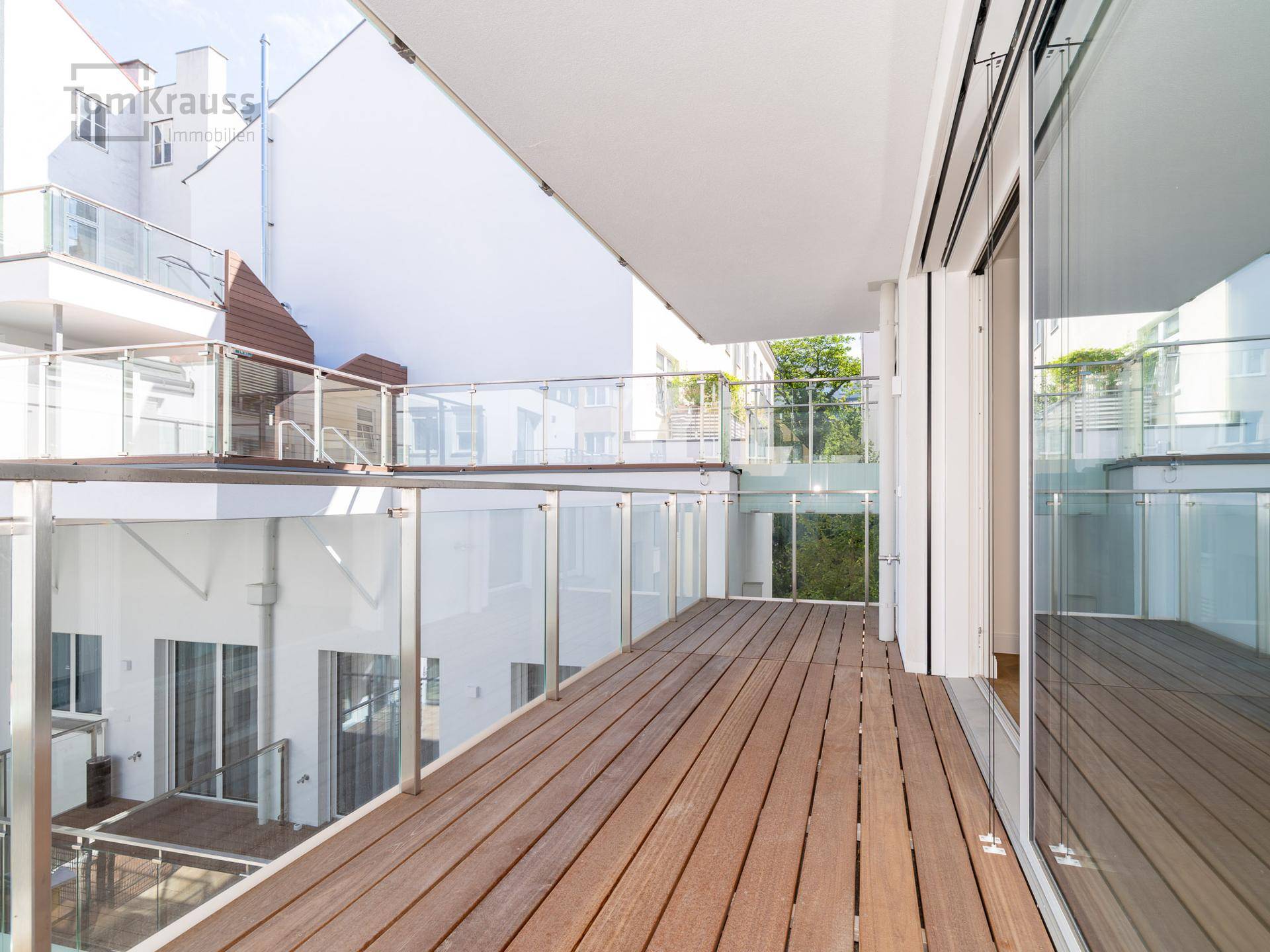 Geräumiger Balkon mit Holzbelag und Glasgeländer, mit Blick auf den Innenhof.