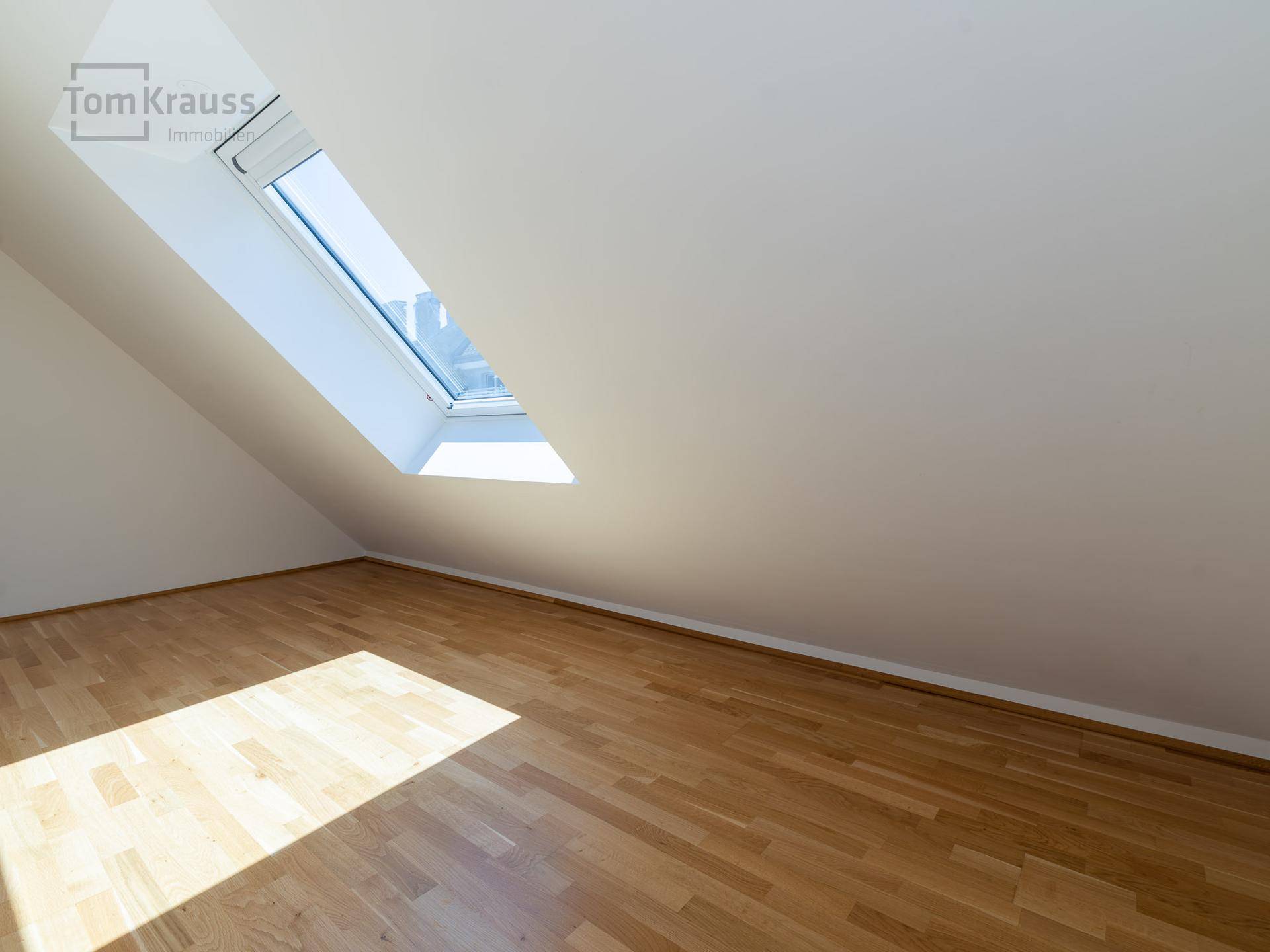 Heller, leerer Raum mit Holzboden und großem Dachfenster, ideal als Arbeitszimmer nutzbar.