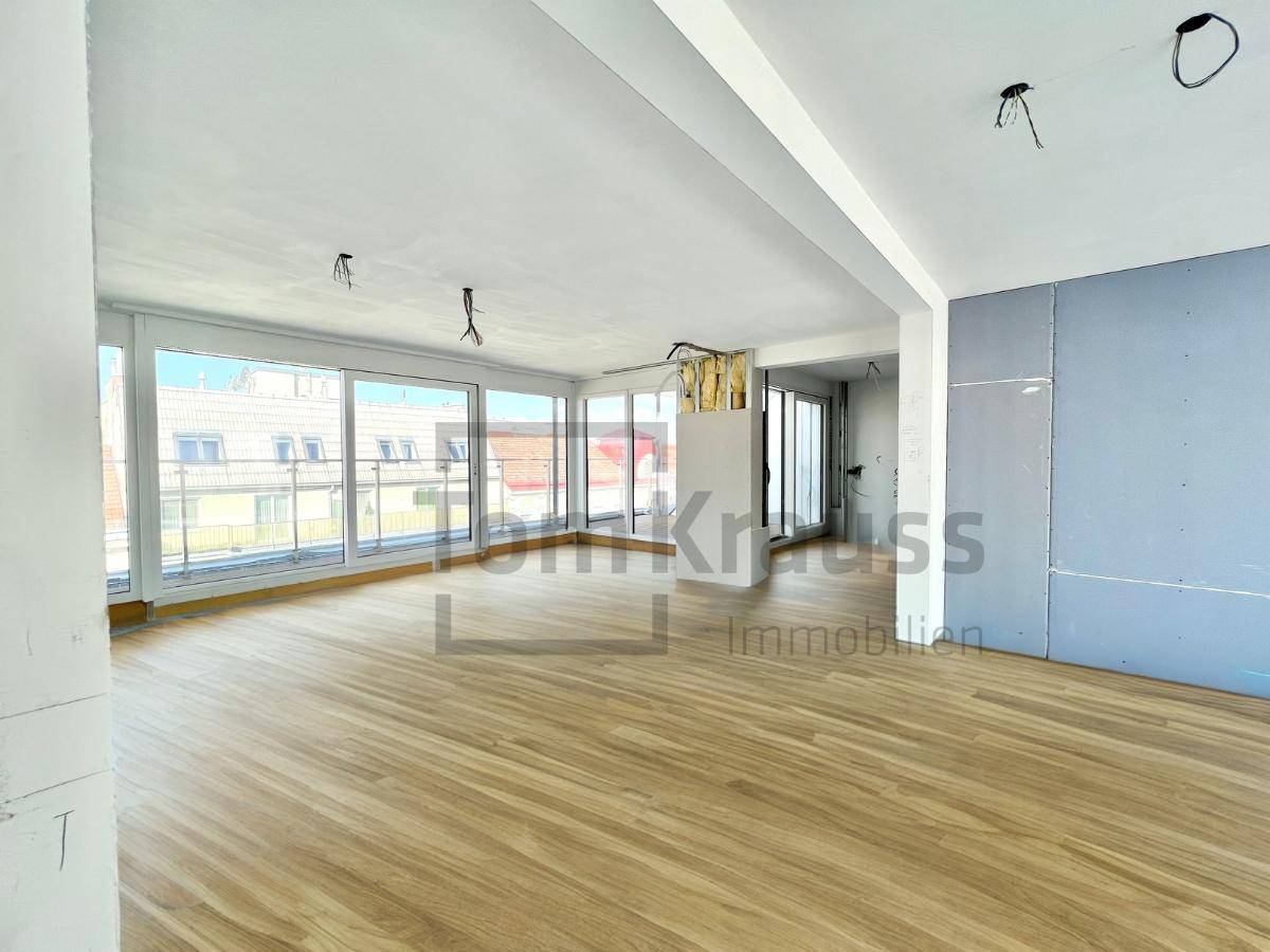 Heller, offener Wohnbereich im Rohbau mit großen Fenstern und neu verlegtem Holzboden.