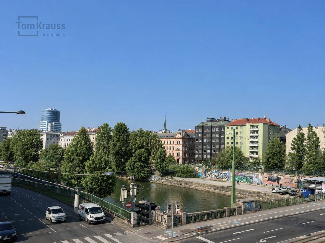 Weitläufiger Blick auf die Stadtlandschaft mit Fluss, Brücke und umliegenden Gebäuden unter blauem Himmel.