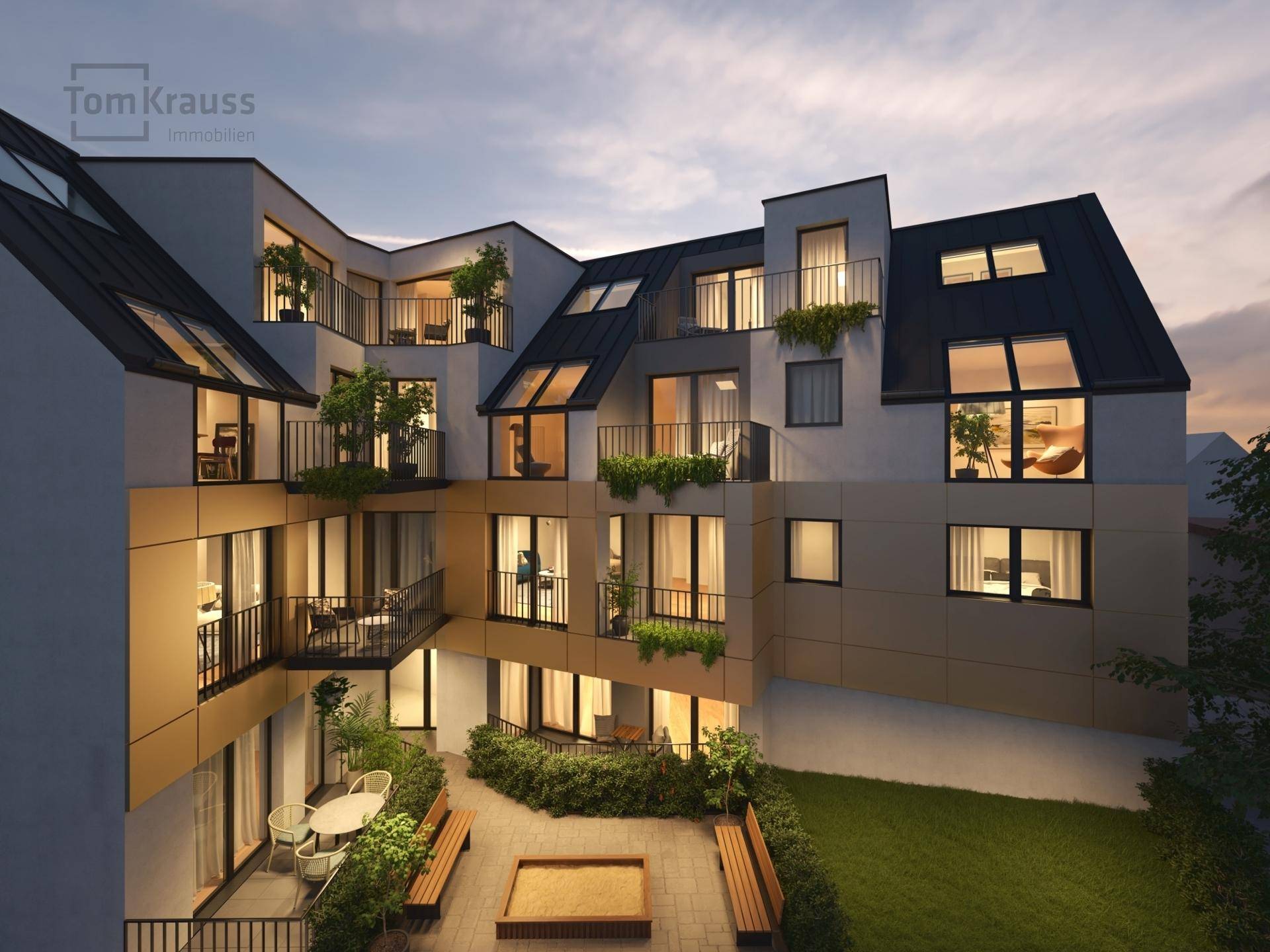 Begrünter Innenhof des Wohnkomplexes mit Sitzbänken und Sandkasten in der Abenddämmerung.