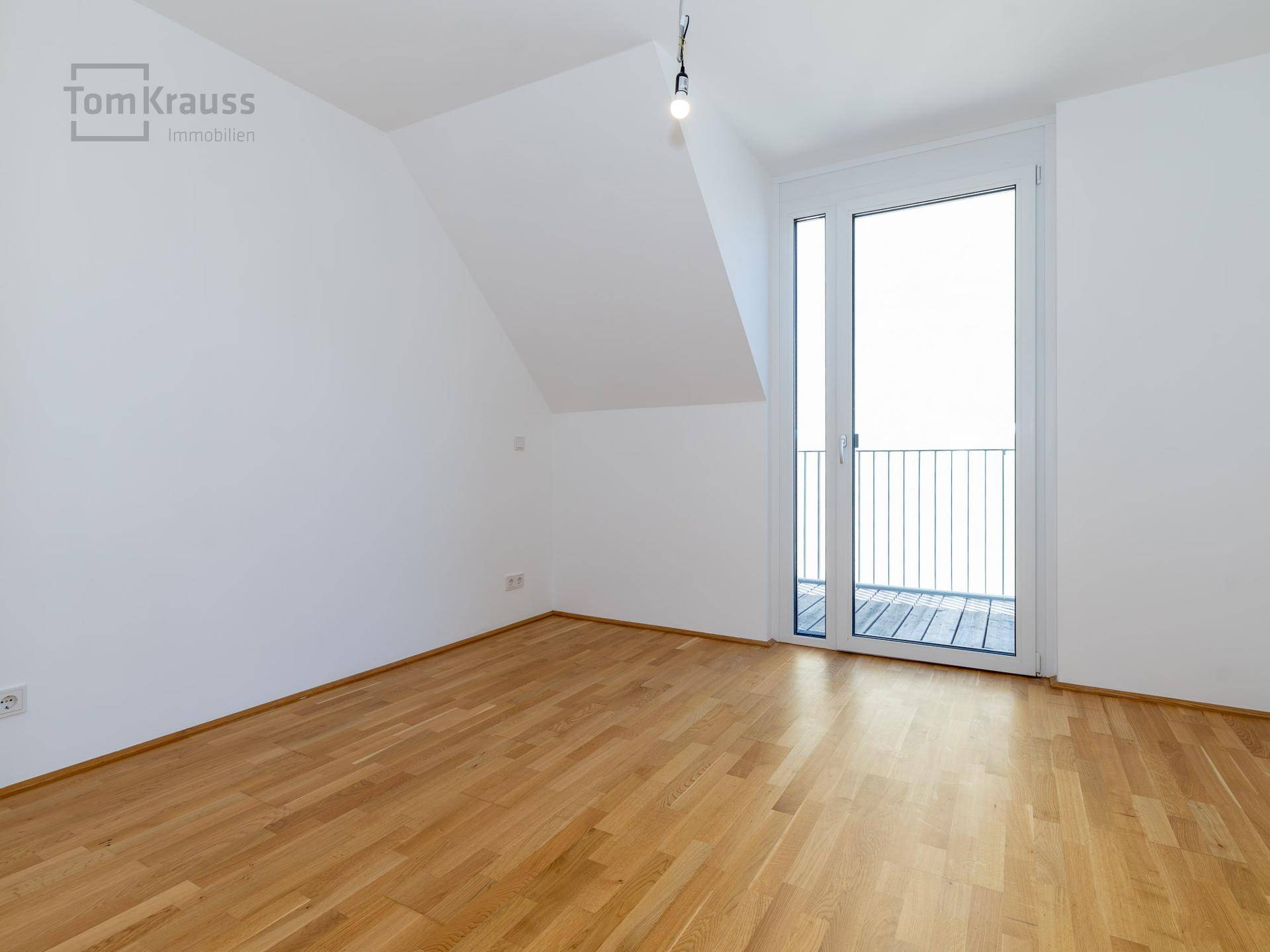 Unmöbliertes Schlafzimmer mit Holzboden und Zugang zu einem Balkon, ideal für ein Kinderzimmer.