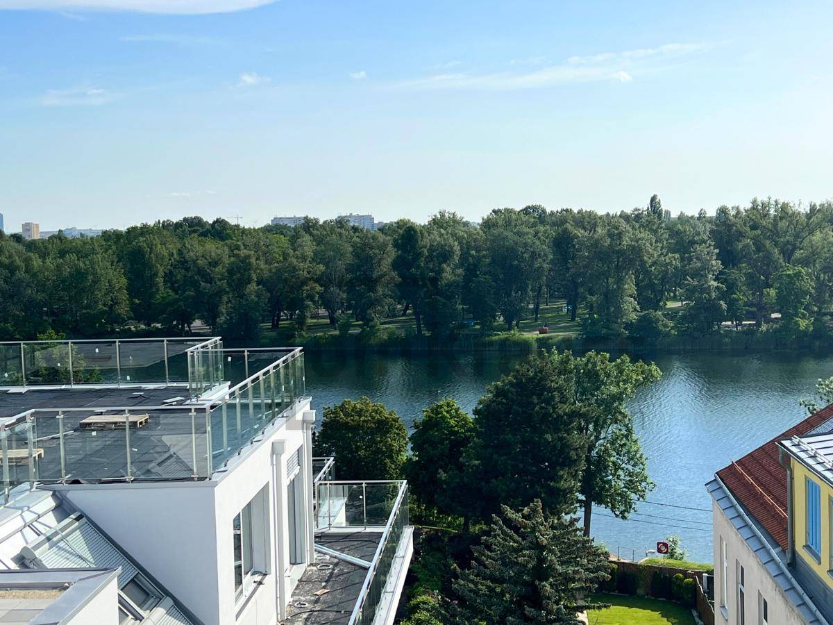 Panoramablick auf einen ruhigen See umgeben von üppigem Grün und Bäumen.