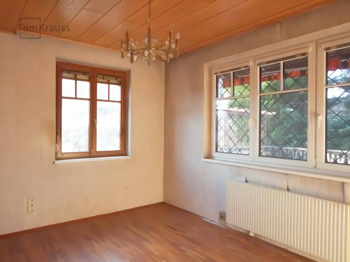 Leeres Zimmer mit Parkettboden, Holzdecke und zwei Fenstern, bereit für eine Renovierung.