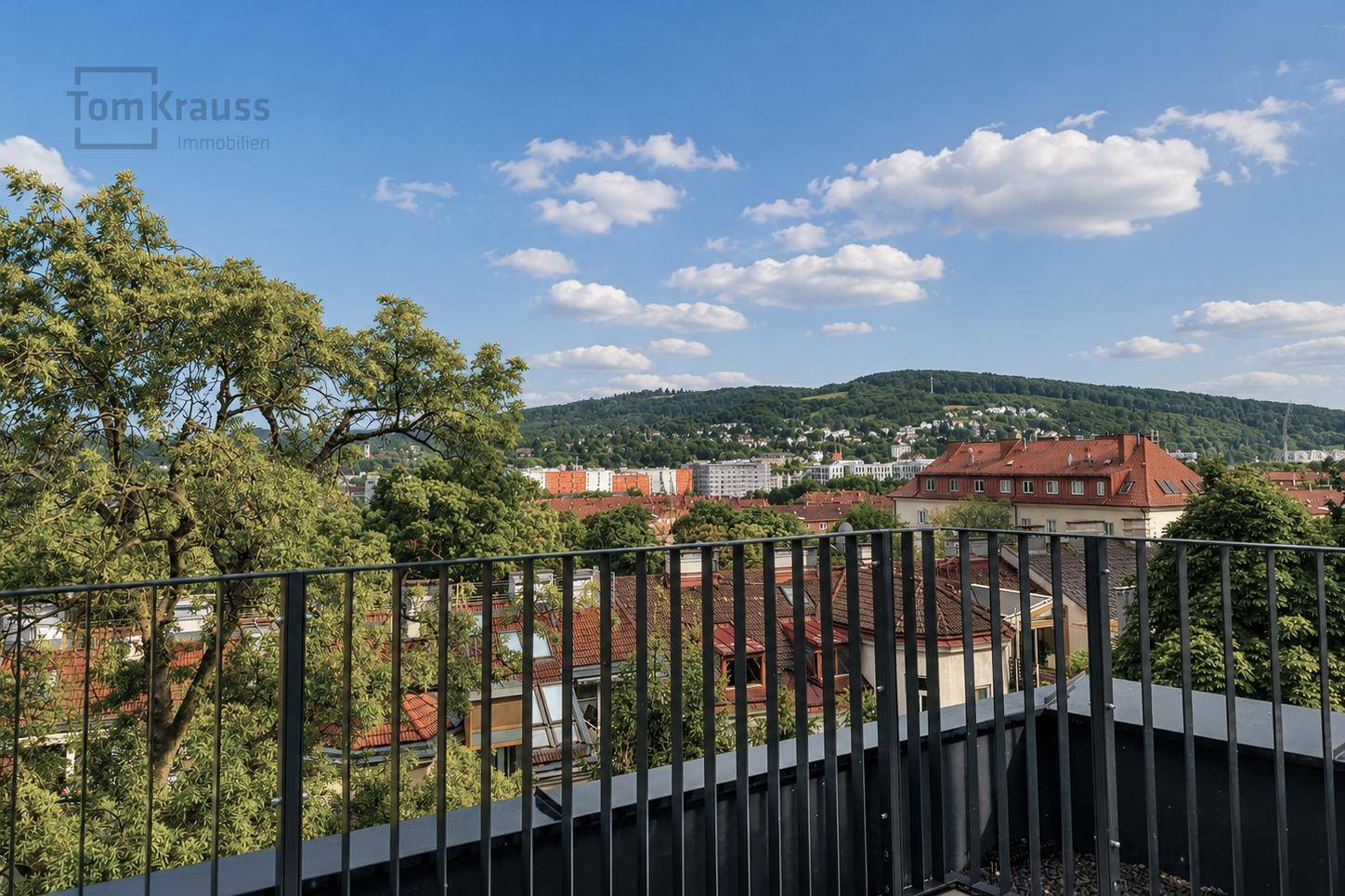 Weitläufiger Blick über die Stadt und grüne Hügel von einem Balkon.