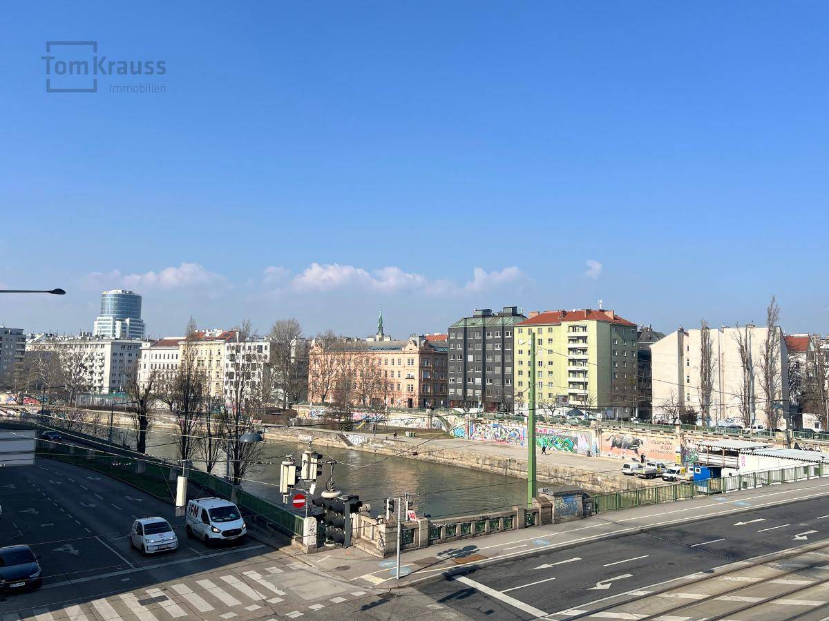 Panoramablick auf die städtische Umgebung mit Fluss, Brücke und Gebäuden unter klarem blauem Himmel.