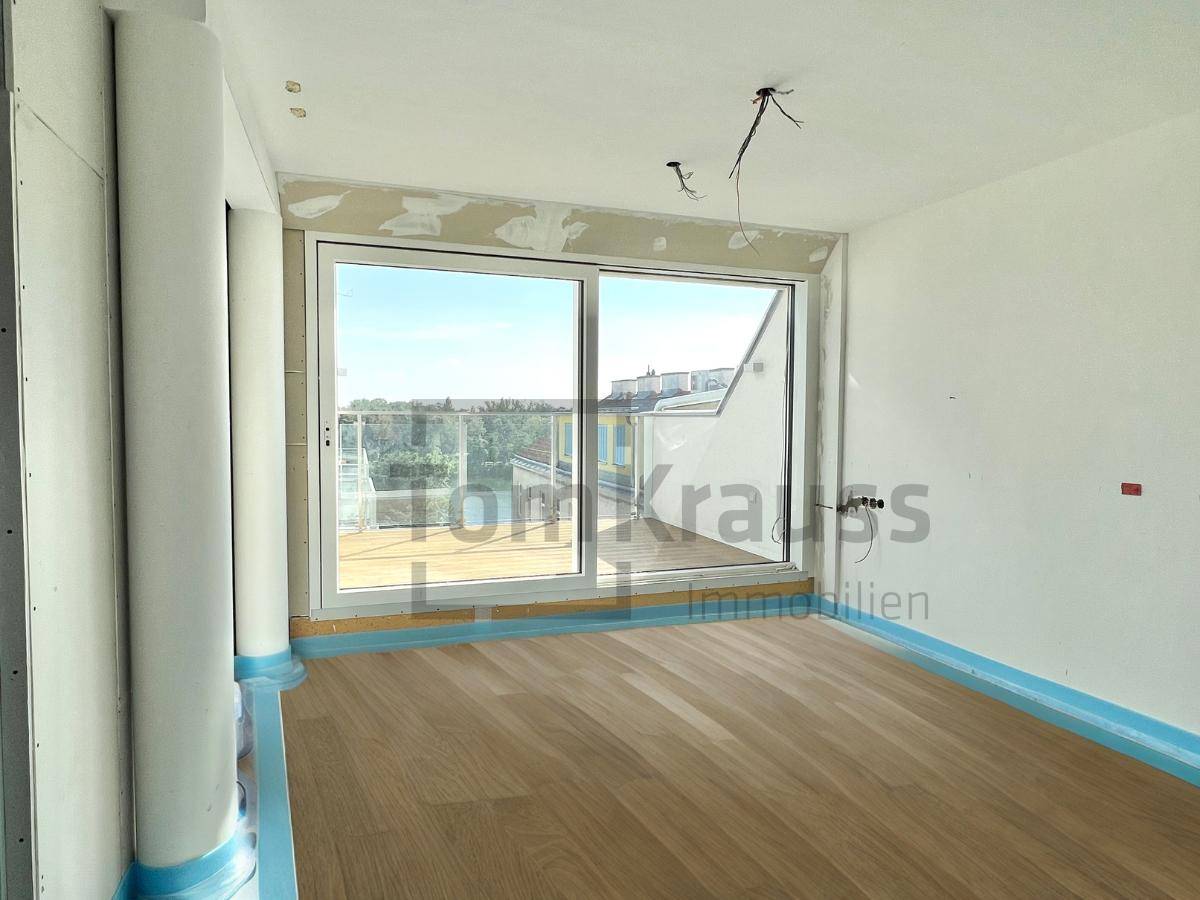Helles Schlafzimmer im Rohbau mit großem Fenster und neuem Holzboden, bereit für den Ausbau.