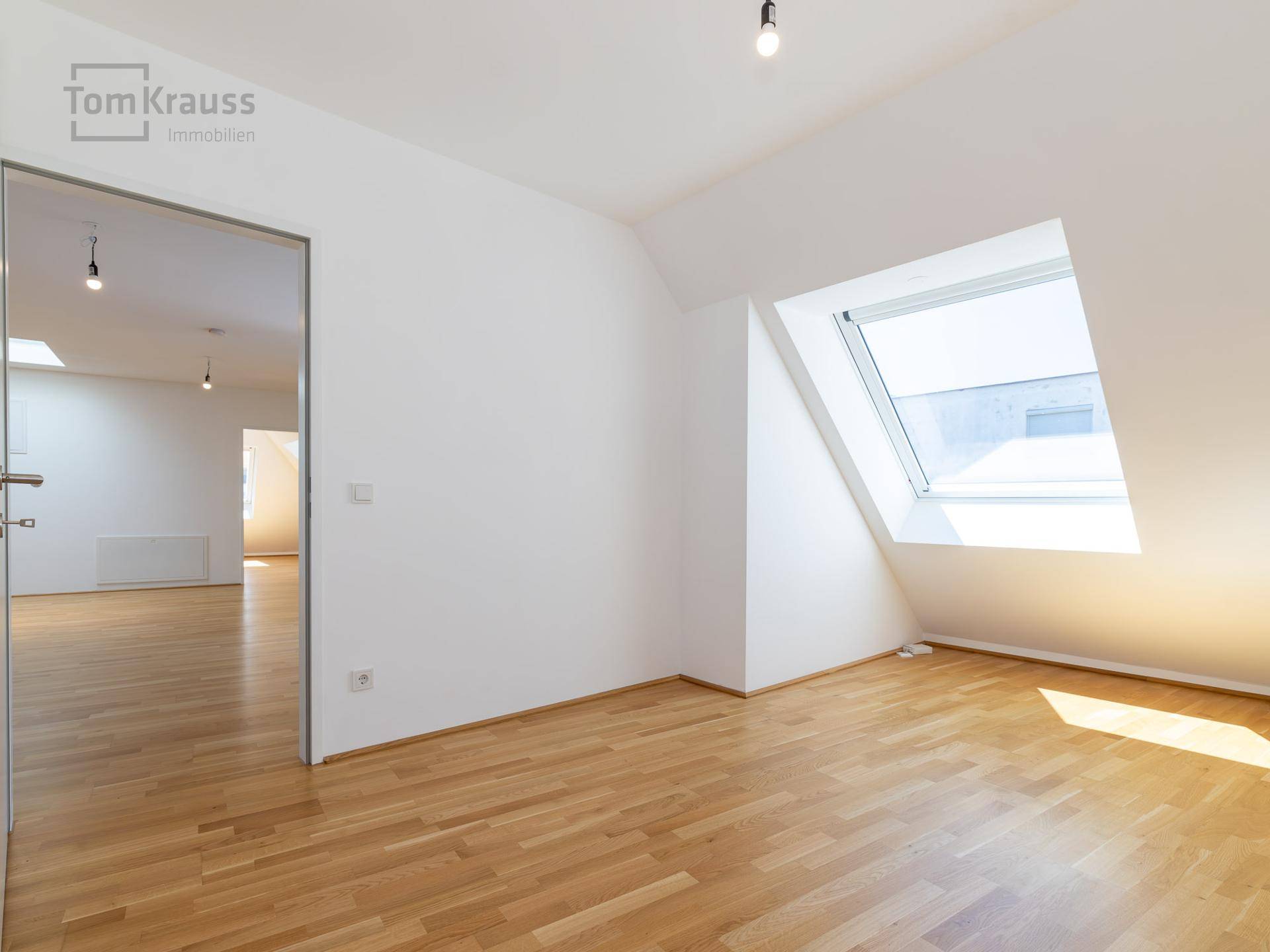 Helles, leeres Schlafzimmer mit Holzboden und großem Dachfenster, bietet viel natürliches Licht.
