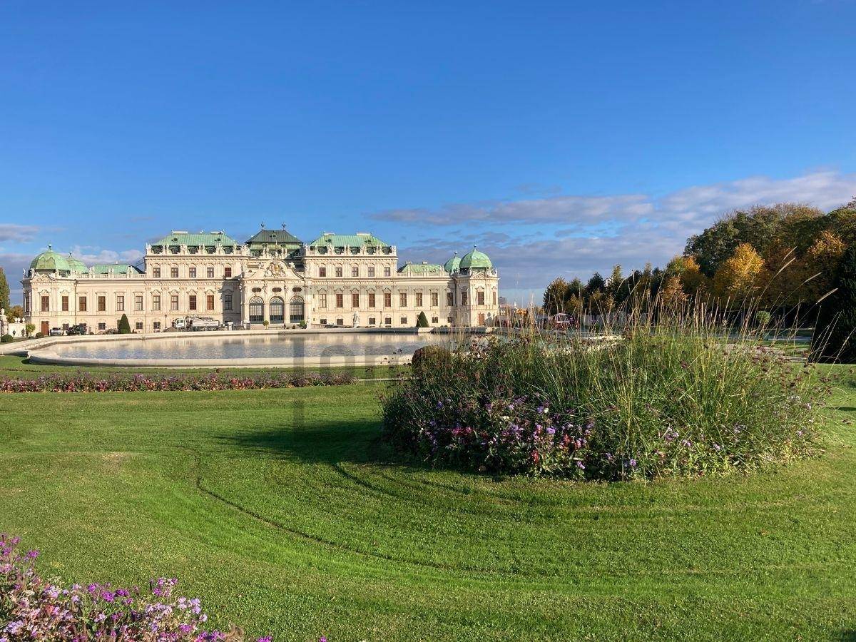 Weitläufiger Garten des Schlosses Belvedere mit Rasenflächen, Blumenbeeten und einem Teich.