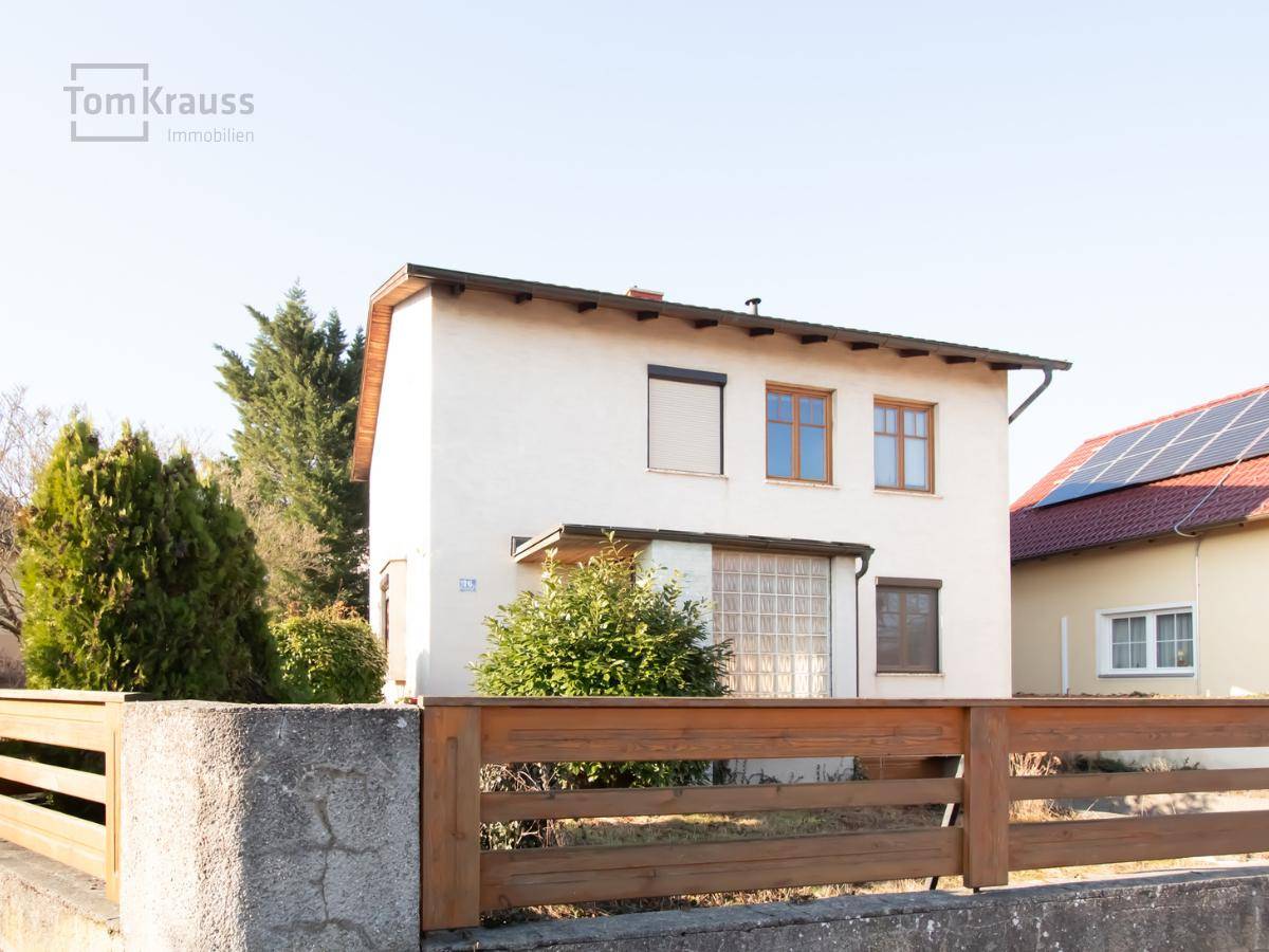 Ansicht des weißen Hauses mit Holzzaun im Vordergrund und einem Nachbarhaus mit Solaranlage.