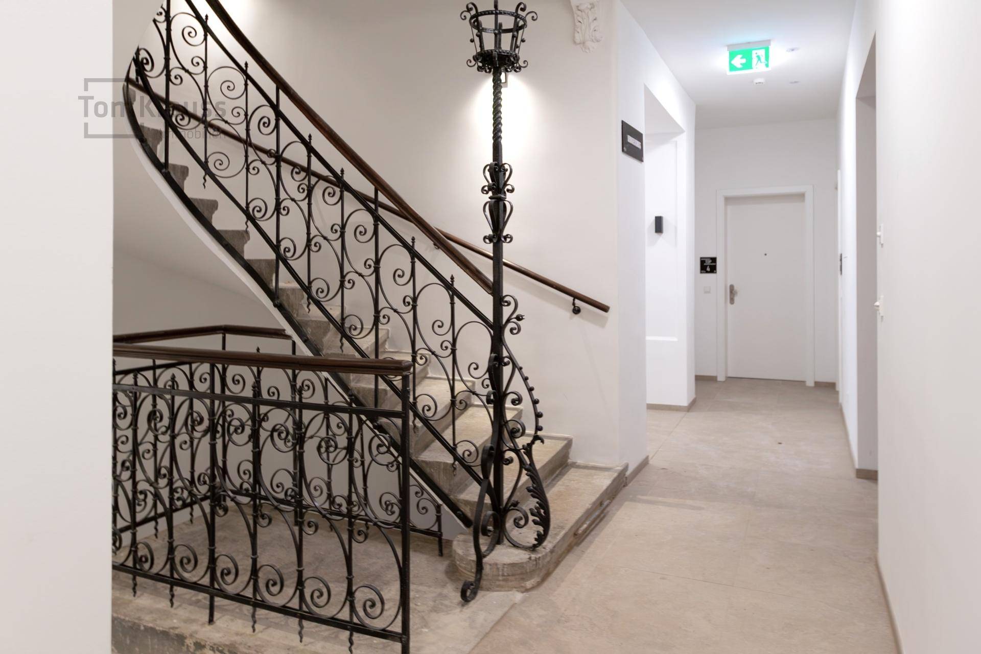 Elegantes Treppenhaus mit schmiedeeisernem Geländer und Steinstufen in einem gepflegten Altbau.