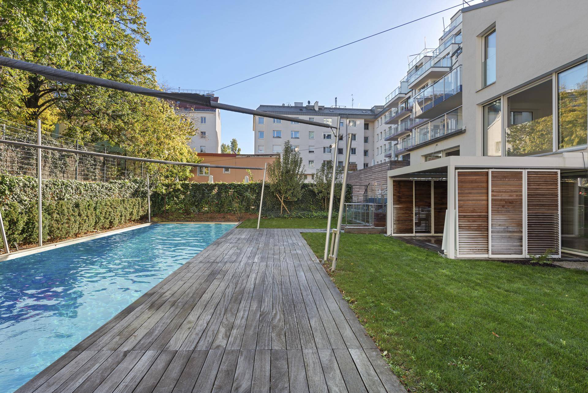 Außenbereich mit Swimmingpool, verwitterter Holzterrasse und gepflegtem Rasen neben dem Gebäude.