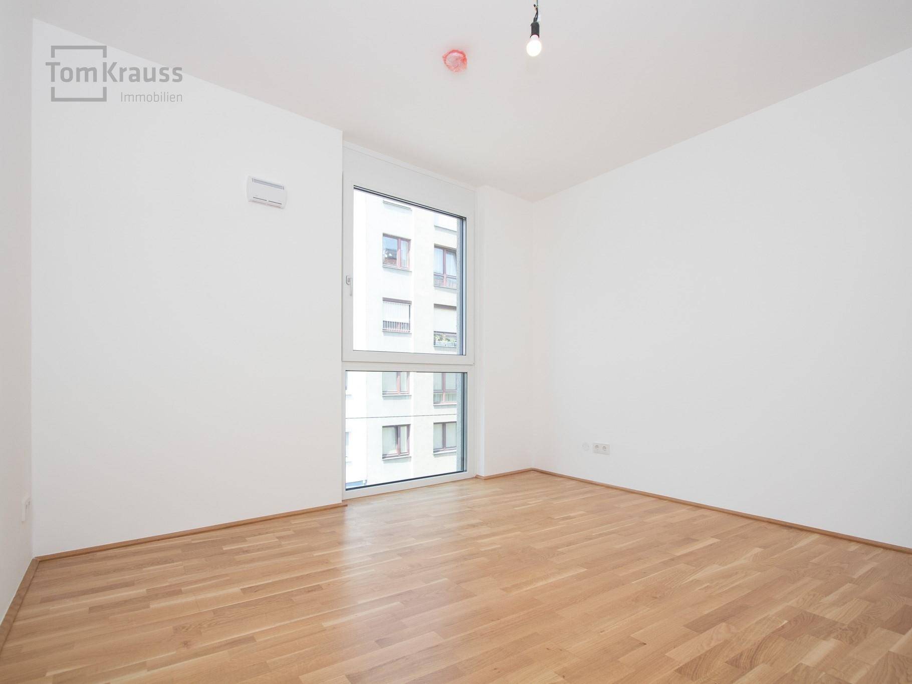 Heller, leerer Raum mit Parkettboden und großem Fenster, bietet einen Blick auf die Stadt.