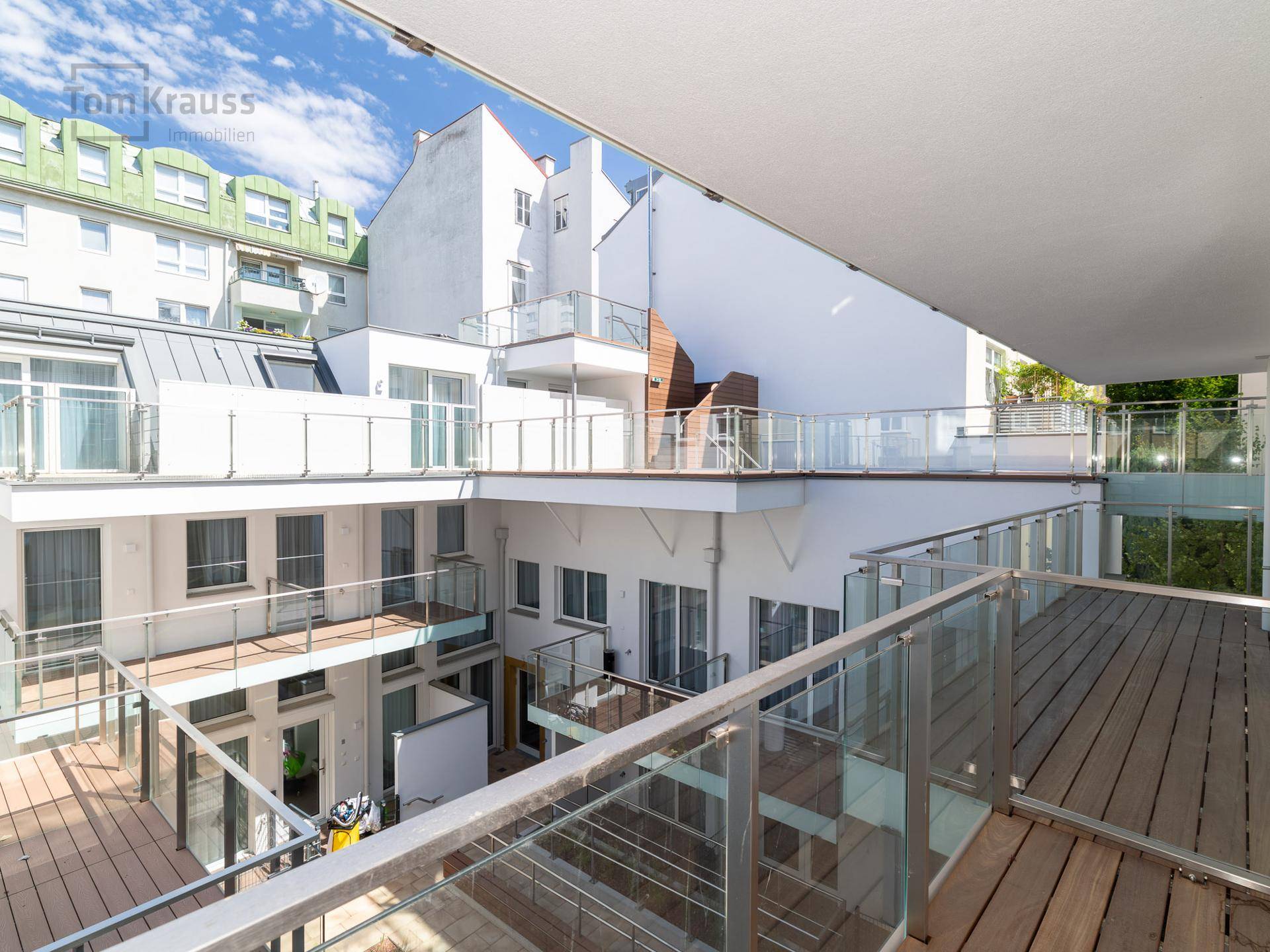Mehrere Balkone mit Glasgeländern und Holzbelag, bieten Ausblick auf den Innenhof.