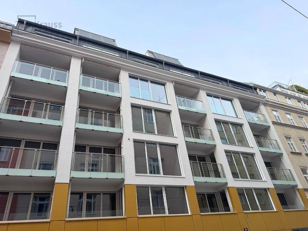 Moderne Wohnhausfassade mit zahlreichen Balkonen und großen Fenstern in städtischer Umgebung.