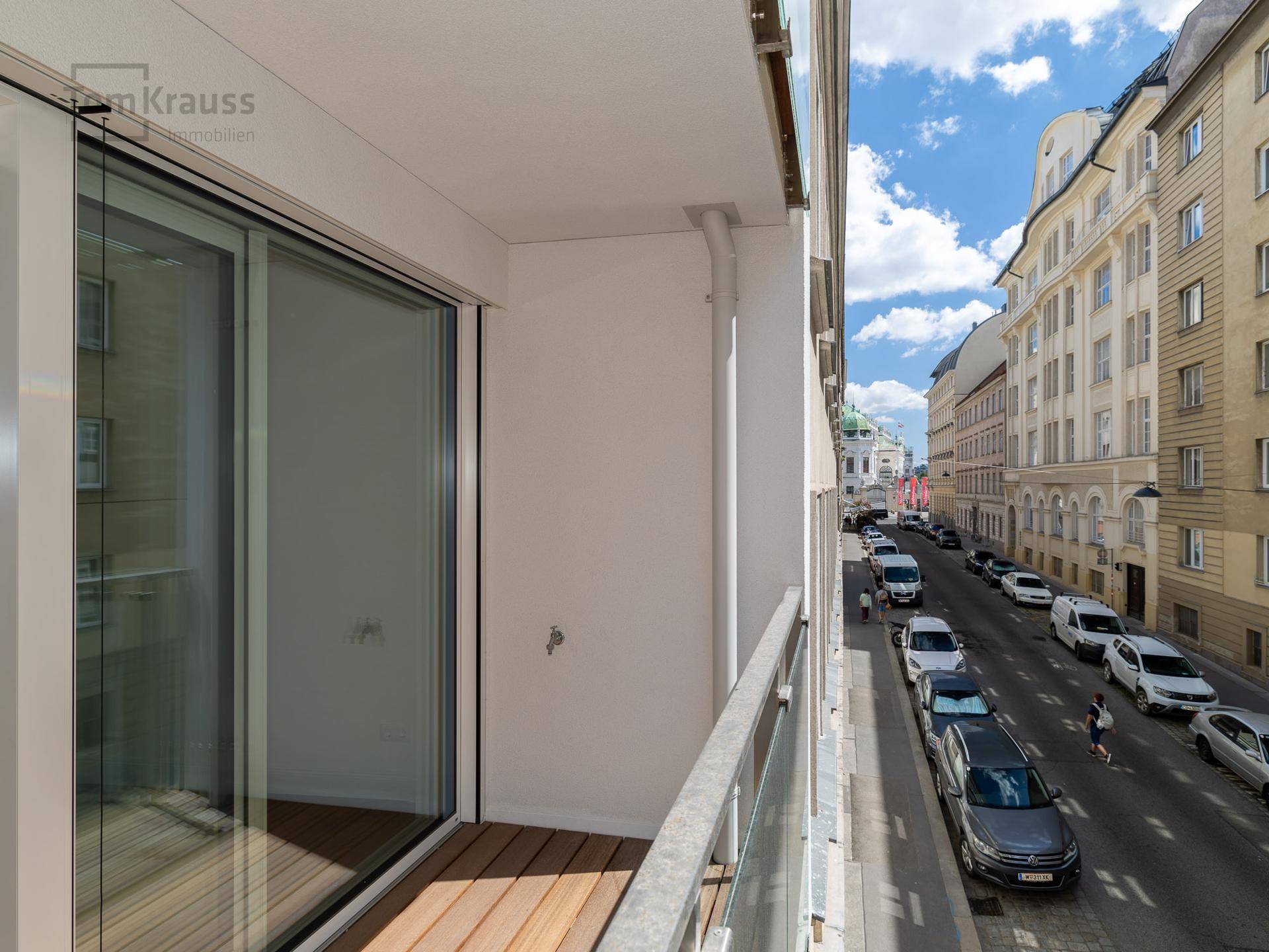 Balkon mit Holzboden und Glasgeländer, bietet einen Blick auf die belebte Stadtstraße.