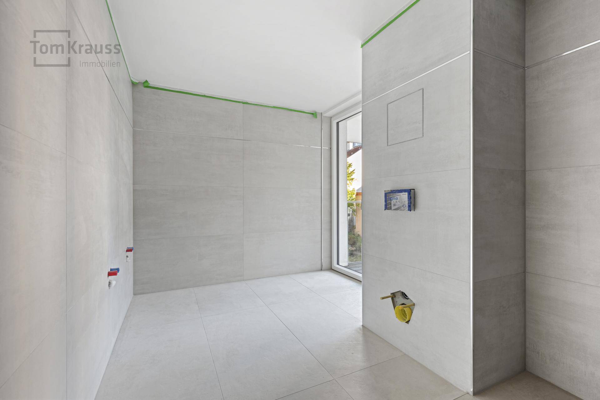 Badezimmer im Bau mit hellen Fliesen und vorbereiteten Anschlüssen für Sanitärobjekte.