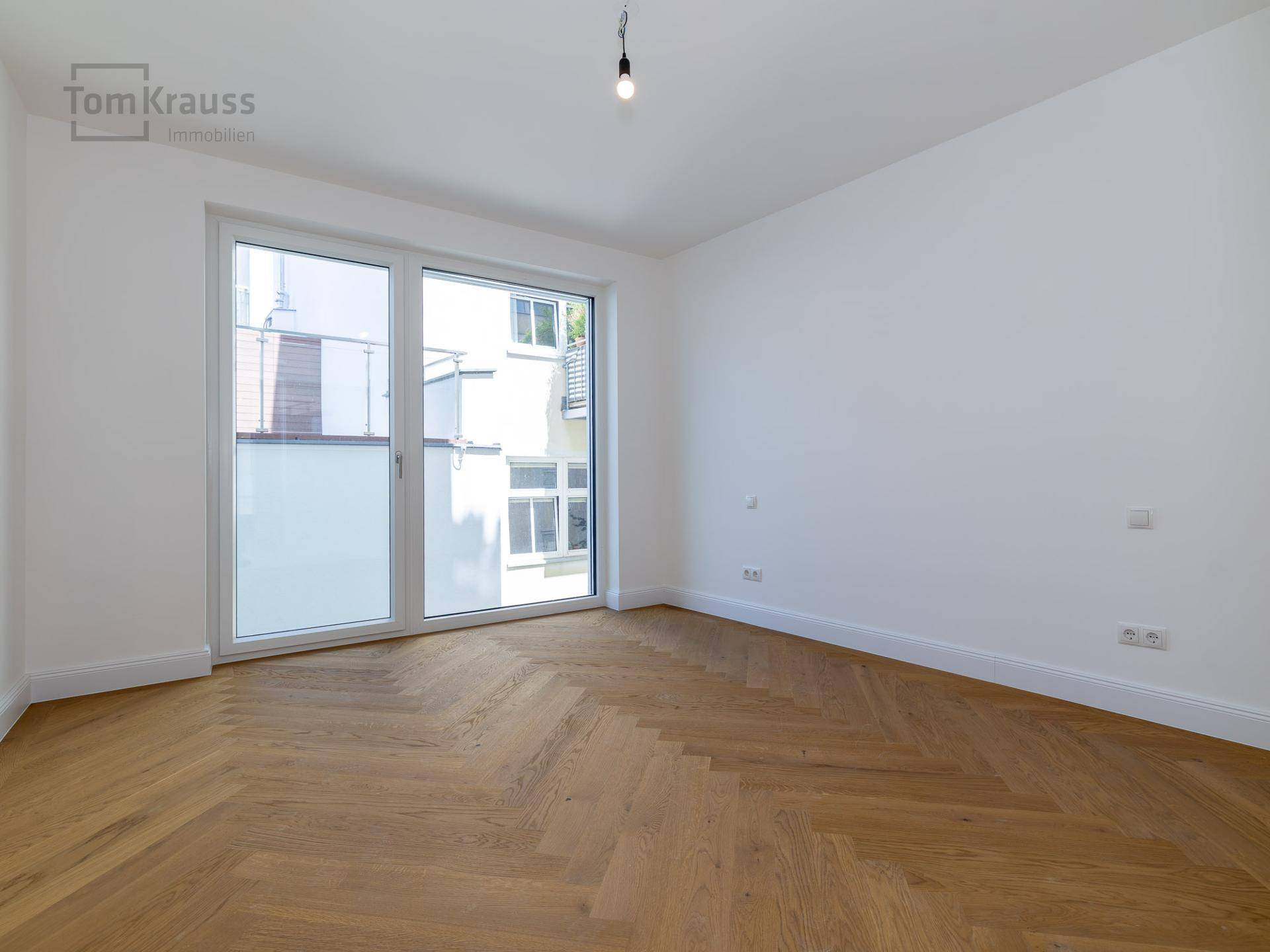 Helles Zimmer mit Fischgrätparkett und großen Fenstern, die einen Blick nach draußen bieten.