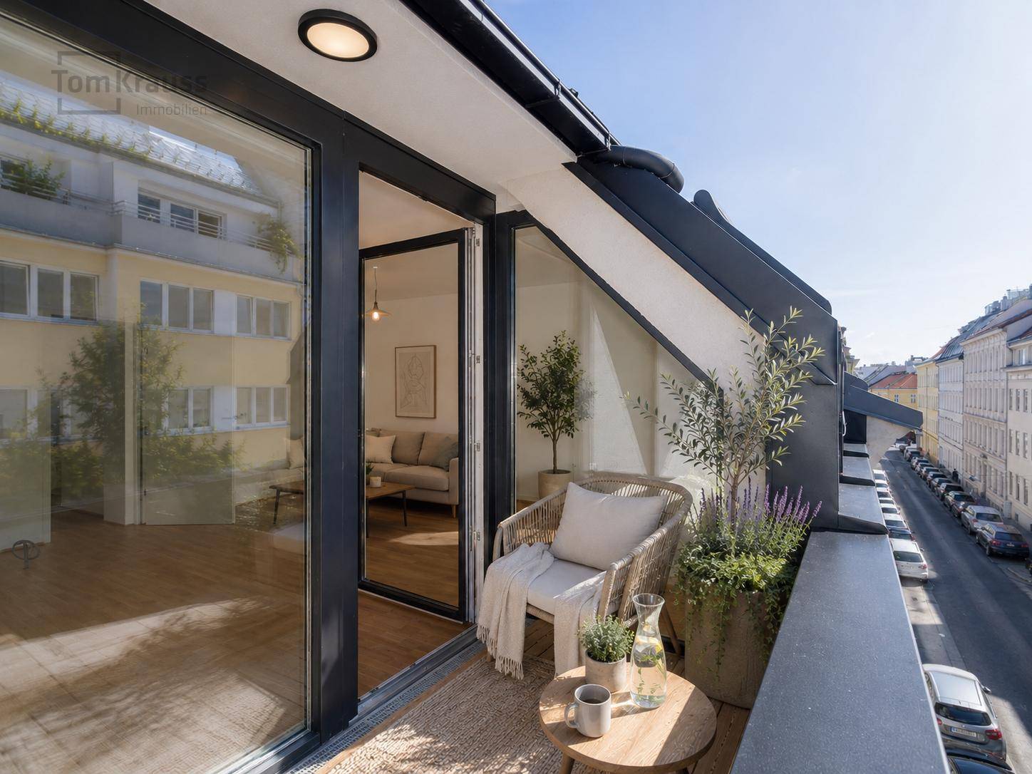 Kleiner, möblierter Balkon mit Holzboden und Blick auf die Straße und umliegende Gebäude.