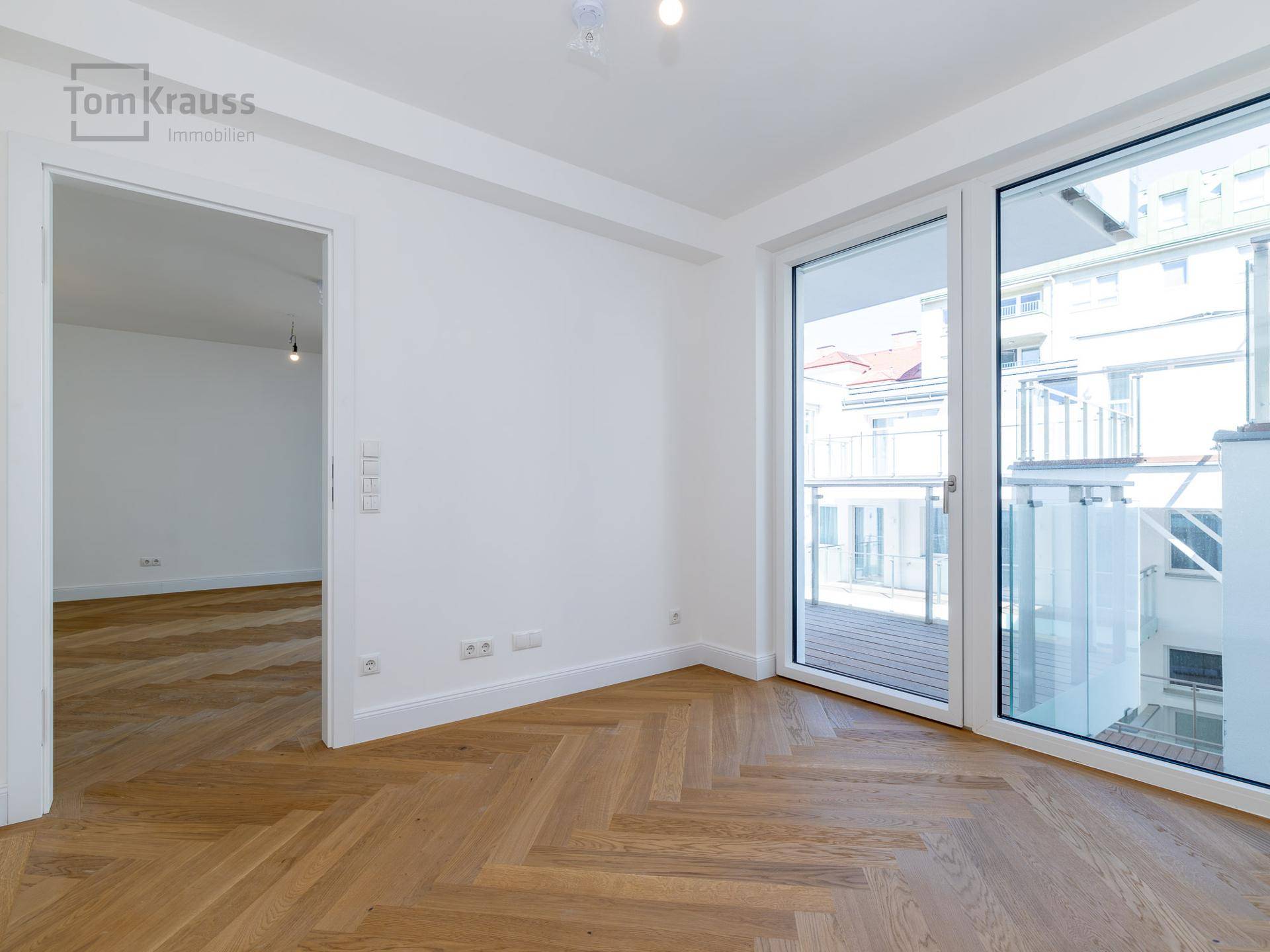 Lichtdurchfluteter Raum mit elegantem Fischgrätparkett und Zugang zum Balkon.
