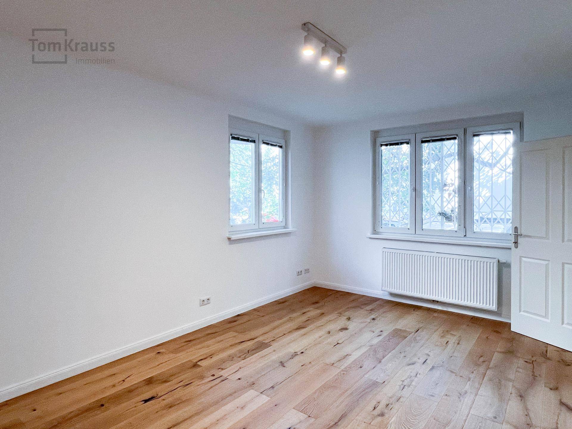 Helles Schlafzimmer mit Holzboden, zwei Fenstern und weißer Heizung.