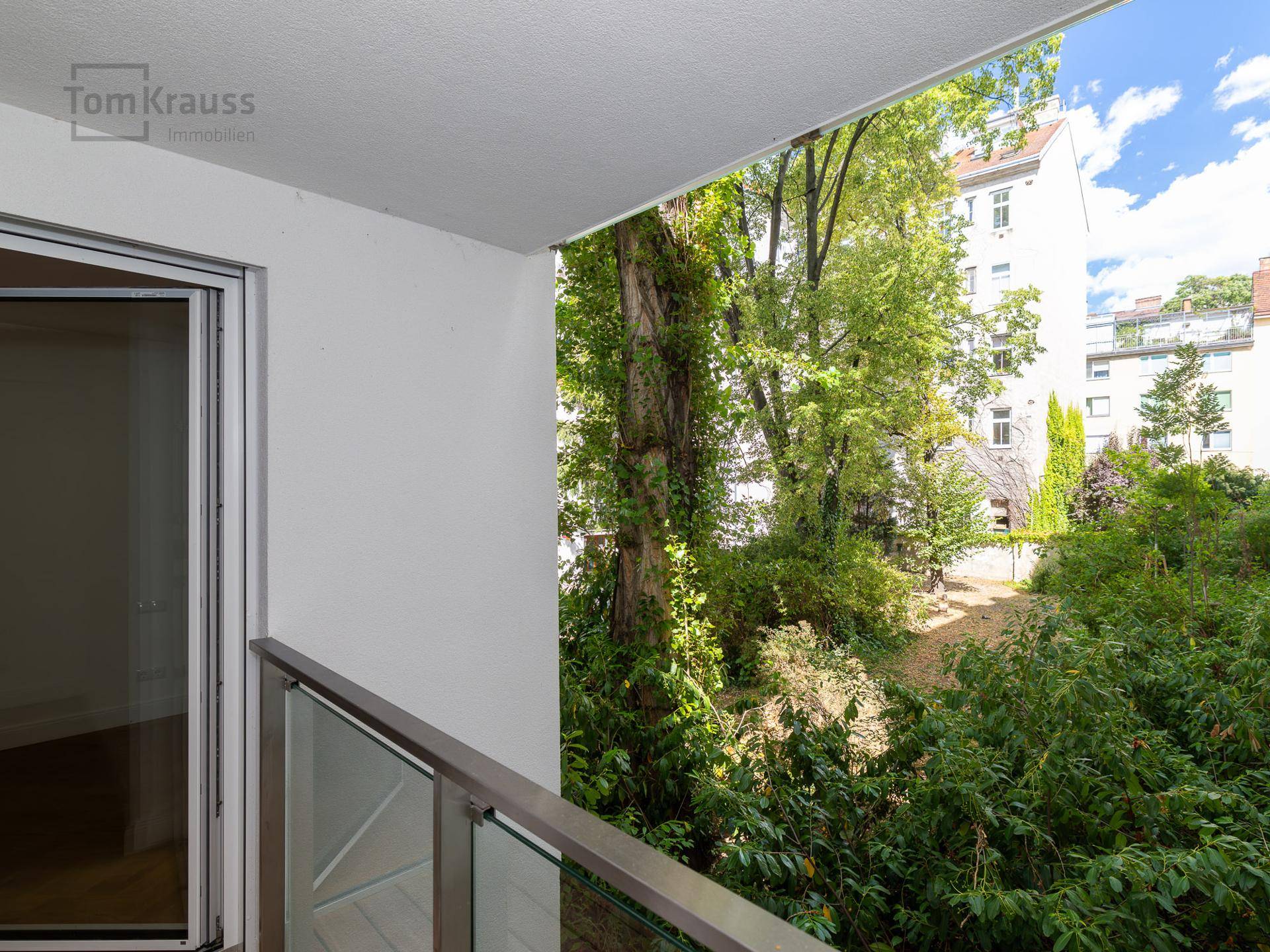 Balkon mit Glasgeländer und Blick auf den grünen Innenhof.
