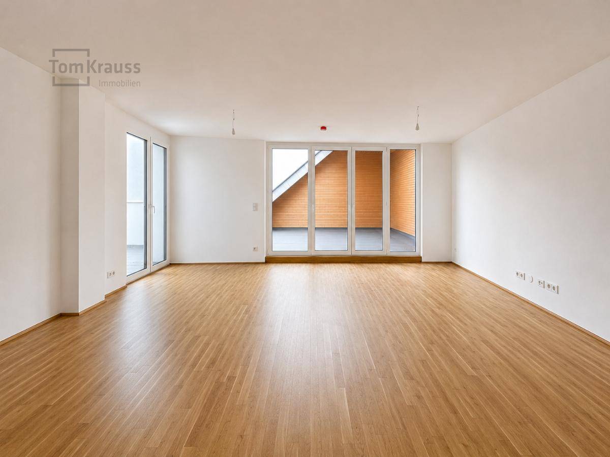 Helles, leeres Wohnzimmer mit Parkettboden und großen Fenstern zum Balkon.