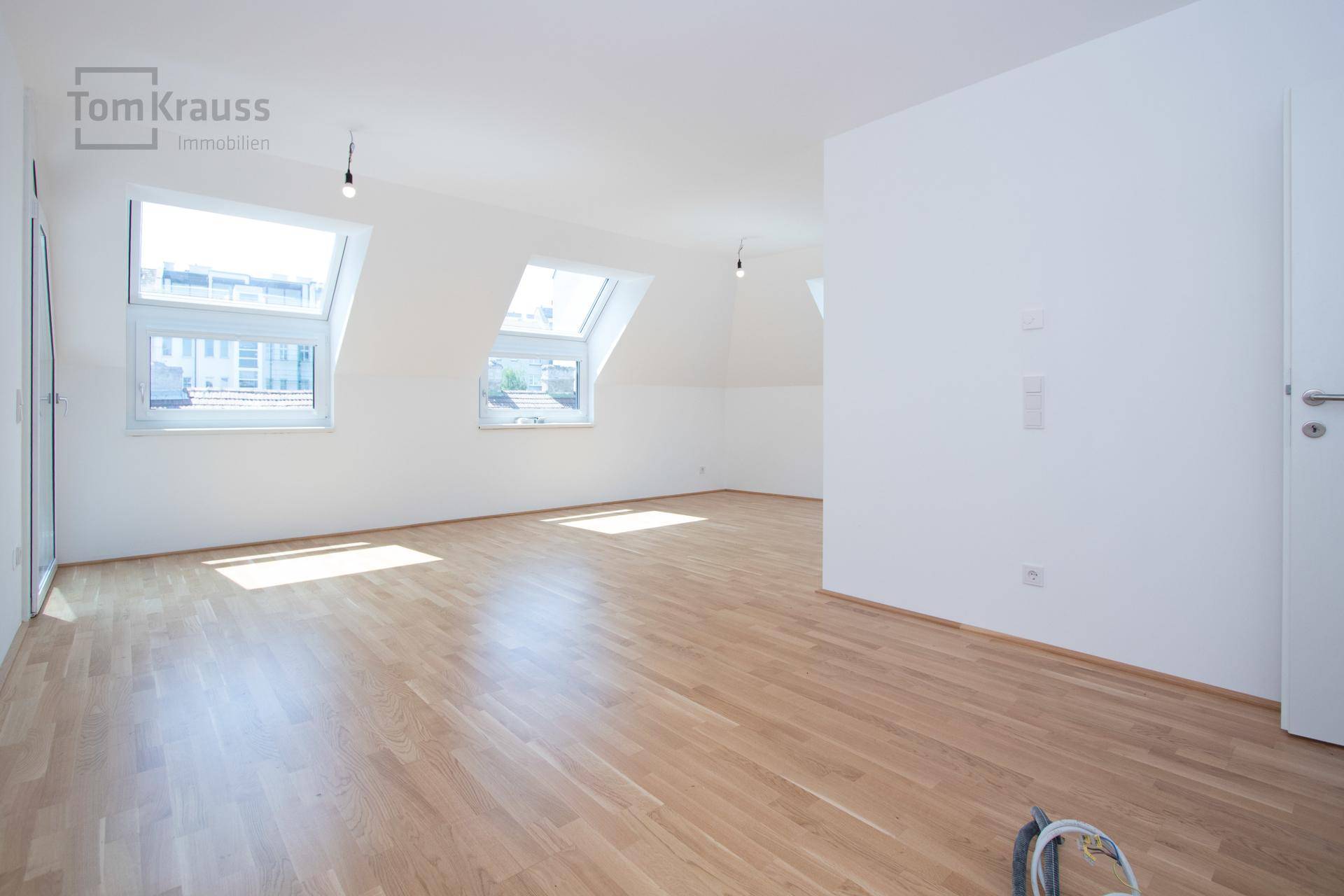 Geräumiges, leeres Wohnzimmer im Dachgeschoss mit Holzparkett und mehreren Dachfenstern.