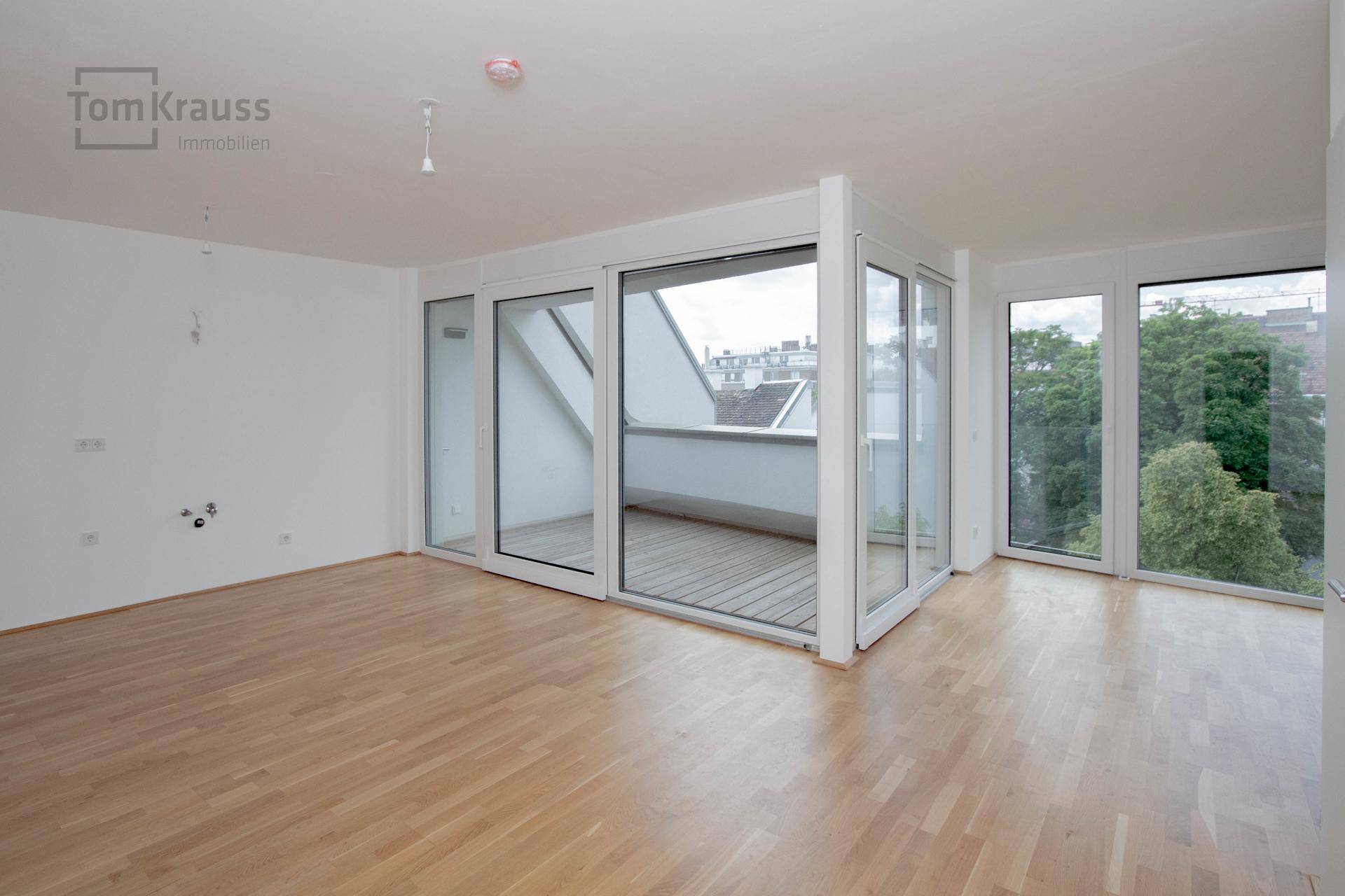 Geräumiger, heller Raum mit Holzboden und großen Schiebetüren zum Balkon oder zur Loggia.