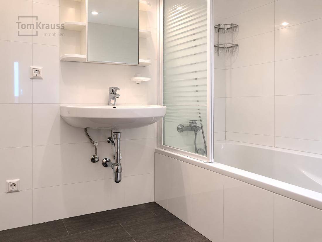 Helles Badezimmer mit Badewanne, Duschabtrennung und Waschbecken, bereit zur Einrichtung.