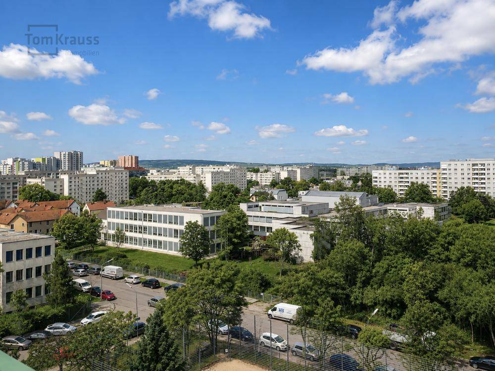 Weitläufiger Blick über die Stadt mit Wohngebäuden und viel Grün unter blauem Himmel.
