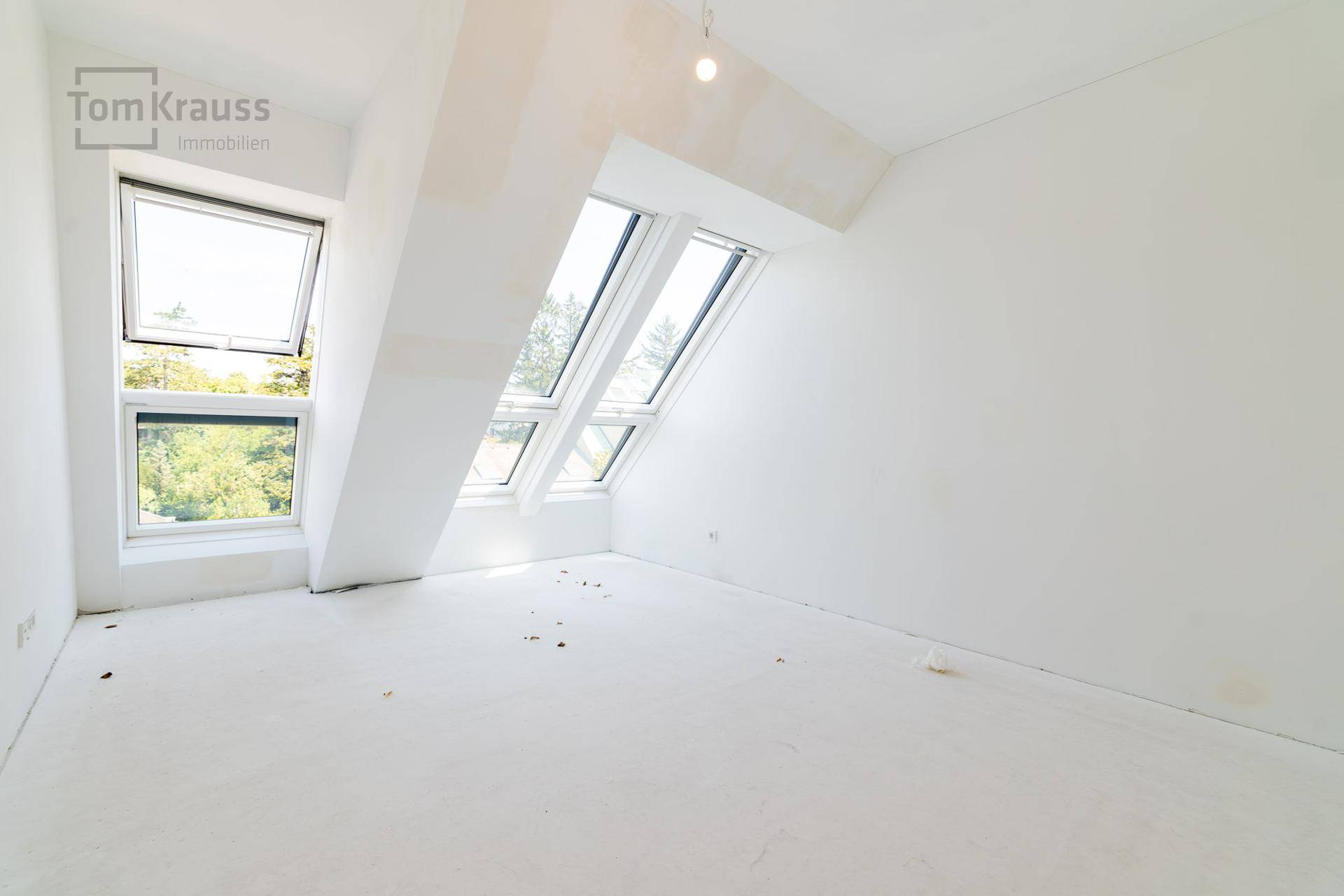 Unmöbliertes Schlafzimmer mit Dachfenstern und Blick ins Grüne, bereit für die Einrichtung.