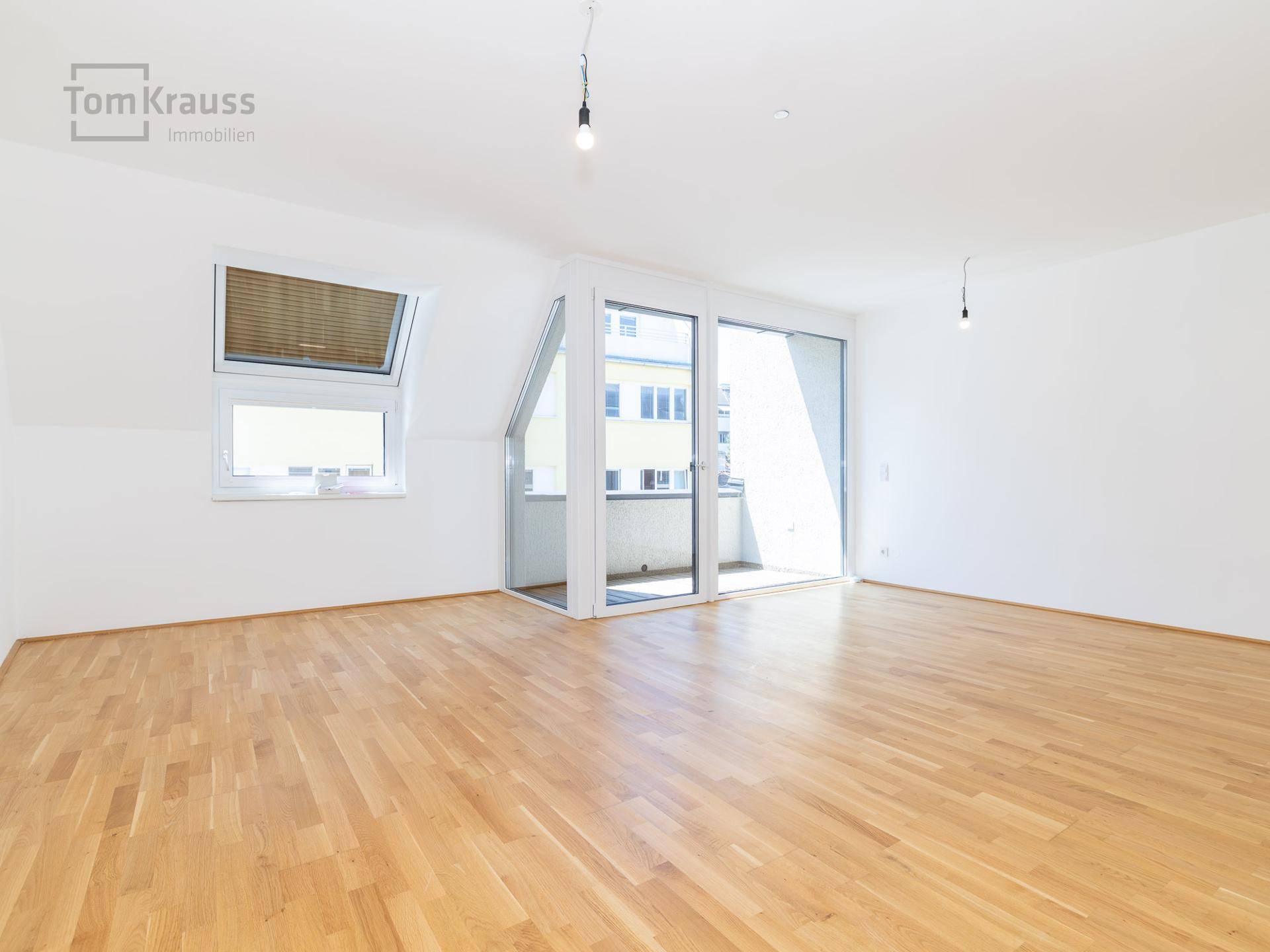 Geräumiges, unmöbliertes Wohnzimmer mit Holzboden und großen Schiebetüren zum Balkon.