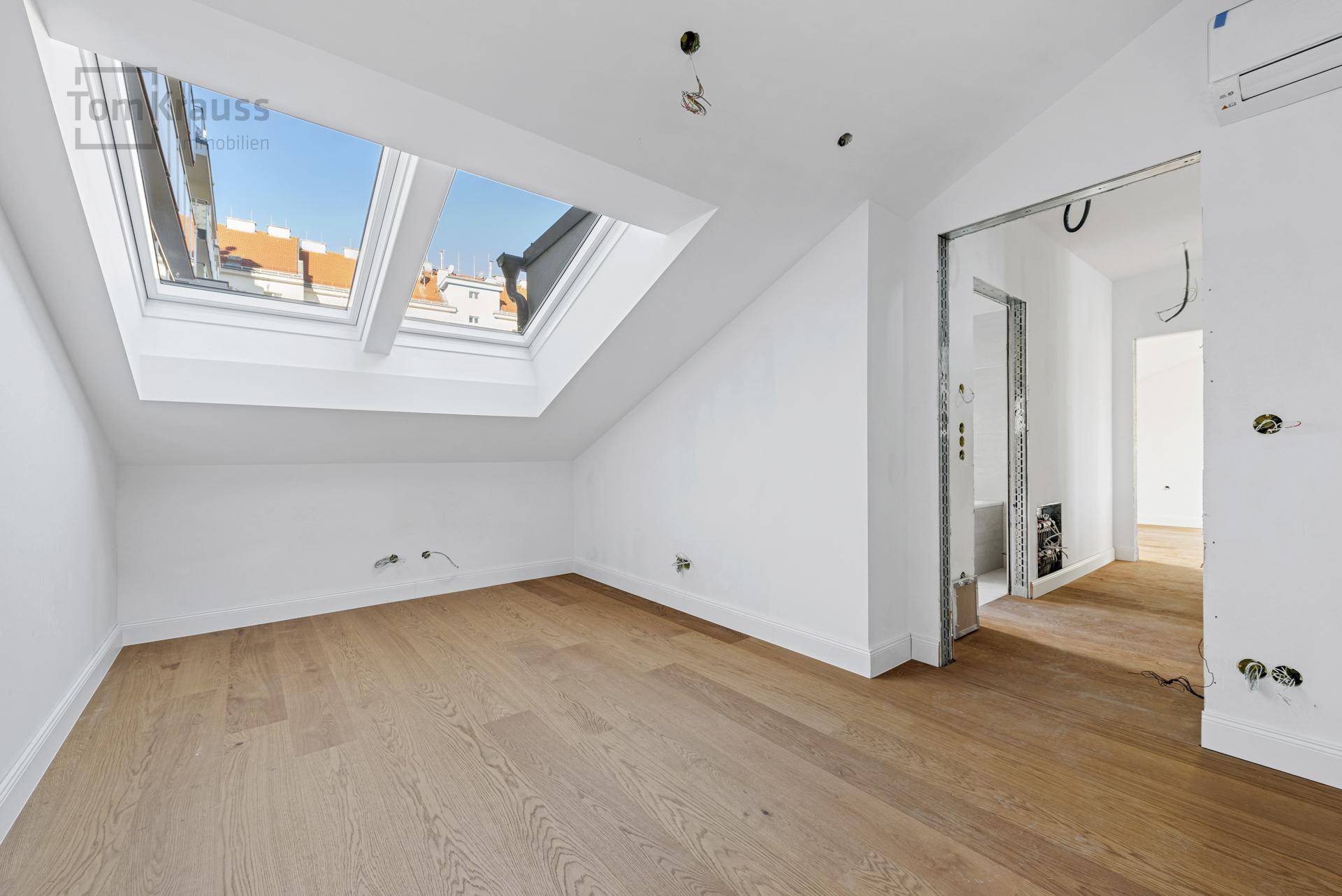 Leeres Schlafzimmer mit Holzboden, Dachschräge und zwei großen Dachfenstern für viel Licht.
