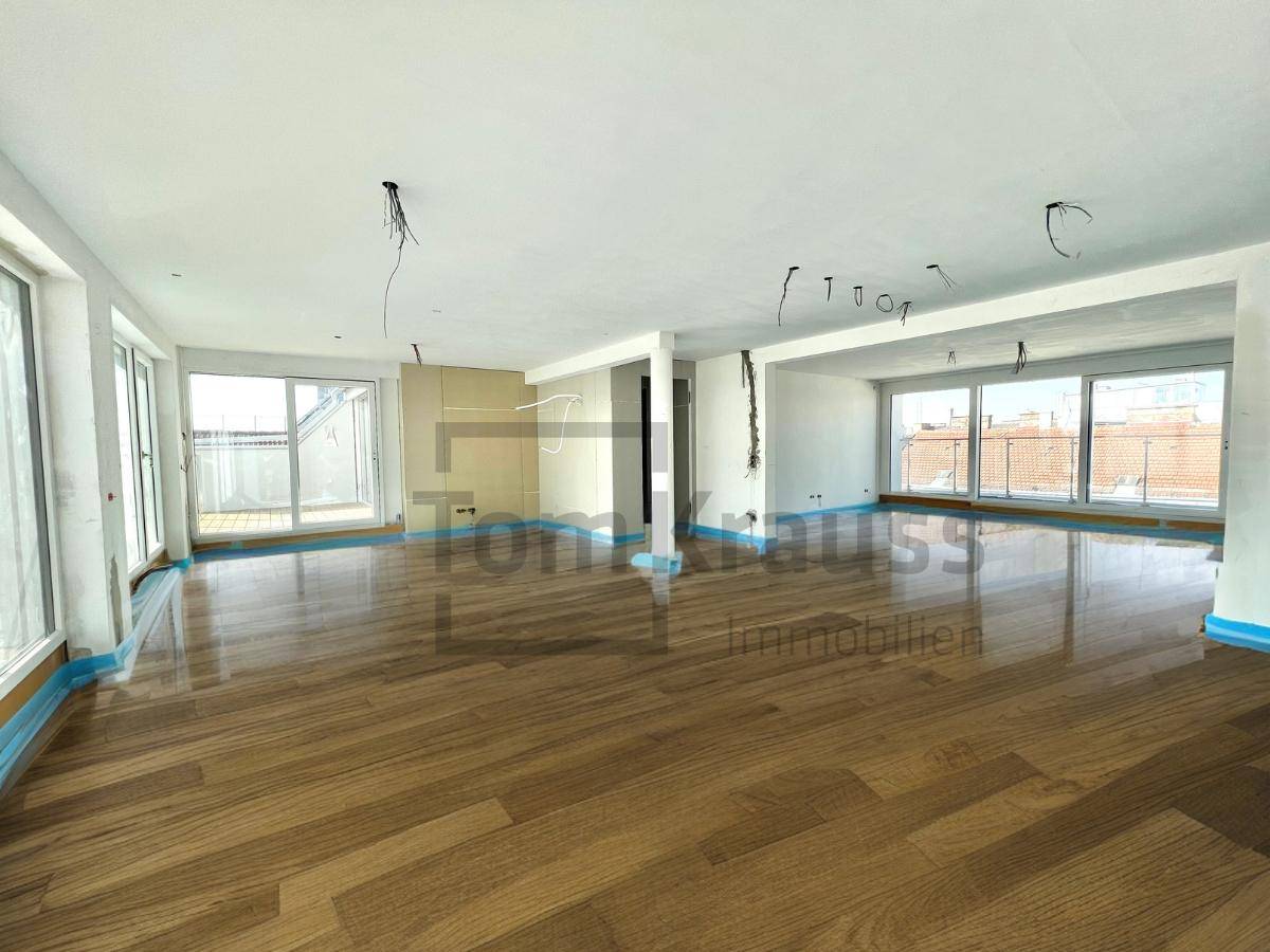 Großer, heller Wohnbereich im Rohbau mit Holzboden und Zugang zu einer Terrasse.