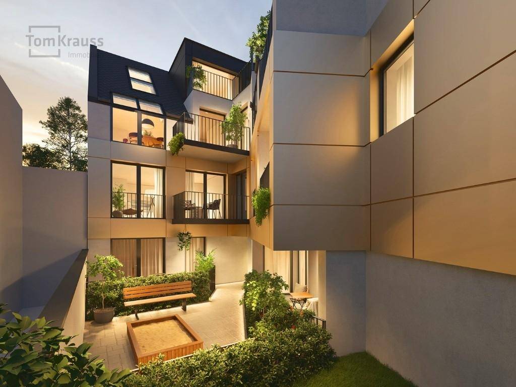 Begrünter Innenhof mit Sitzbank und Sandkasten, umgeben von modernen Gebäudefassaden.