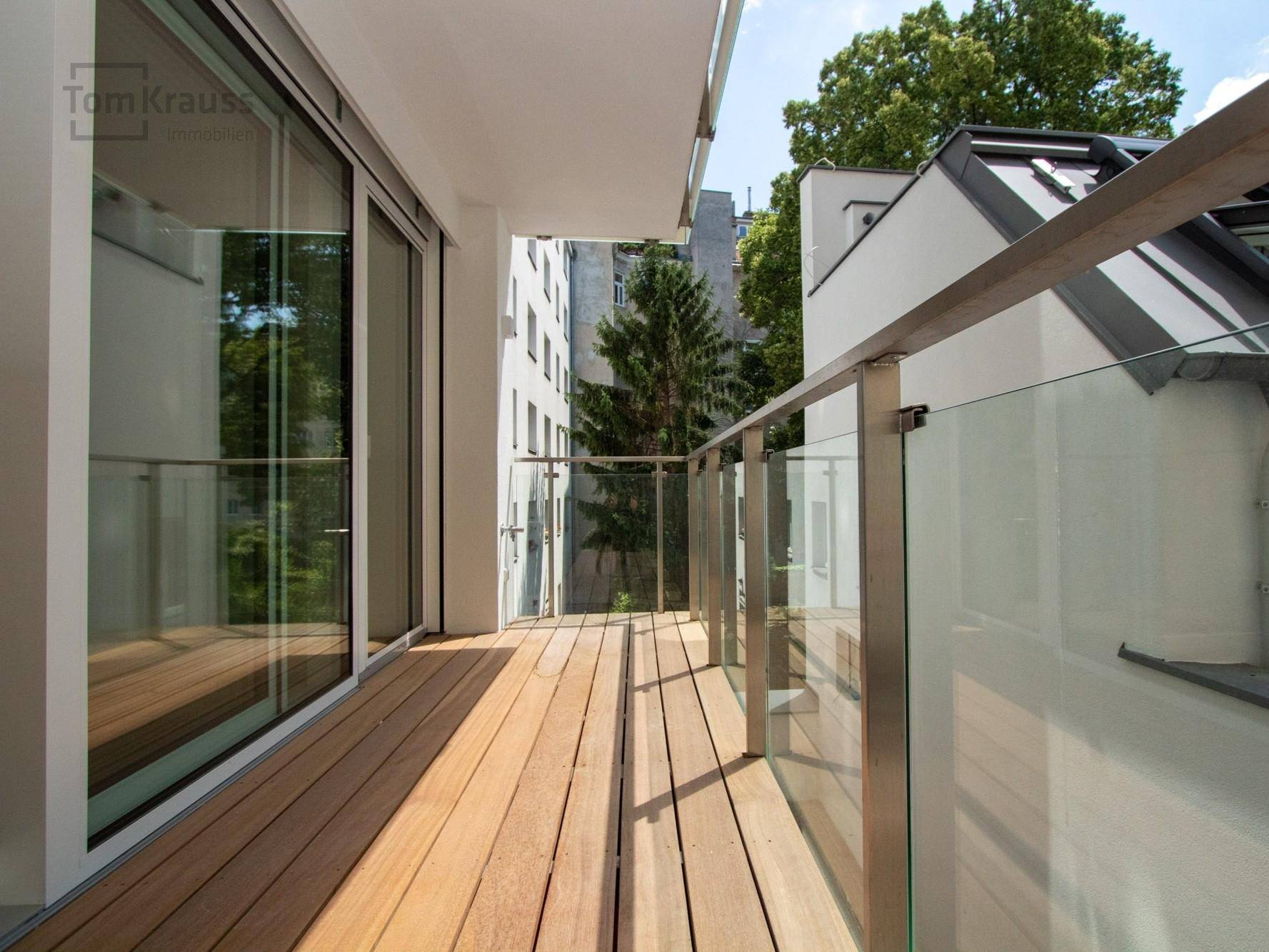 Geräumiger Balkon mit Holzdielenboden und modernem Glasgeländer, ideal für Entspannung im Freien.