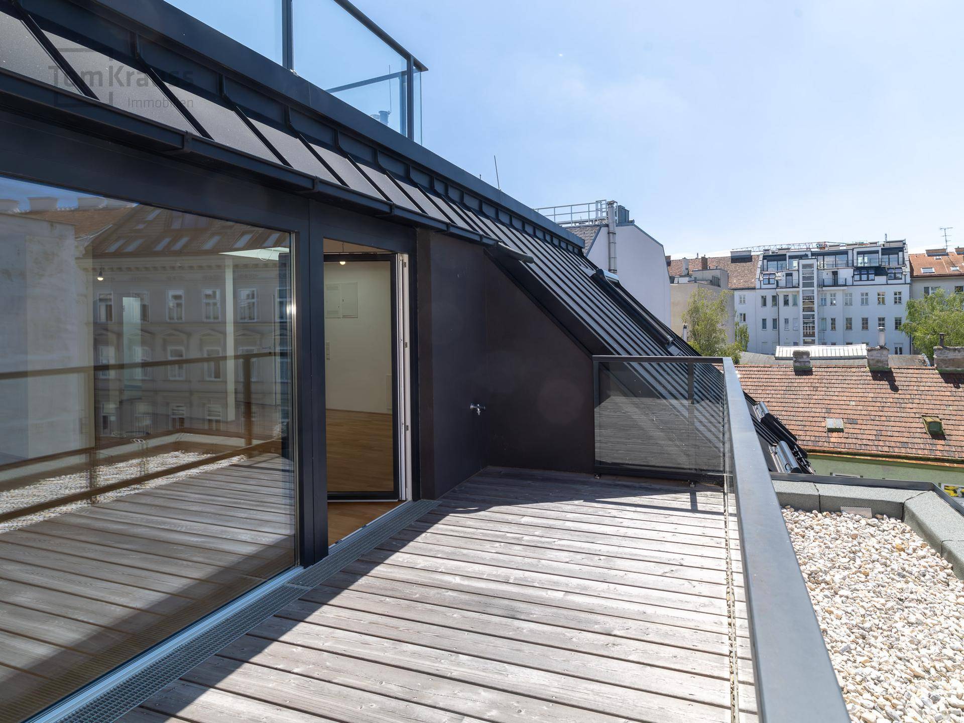 Helle Dachterrasse mit Holzboden und Glasgeländer, bietet direkten Zugang zu den Innenräumen.