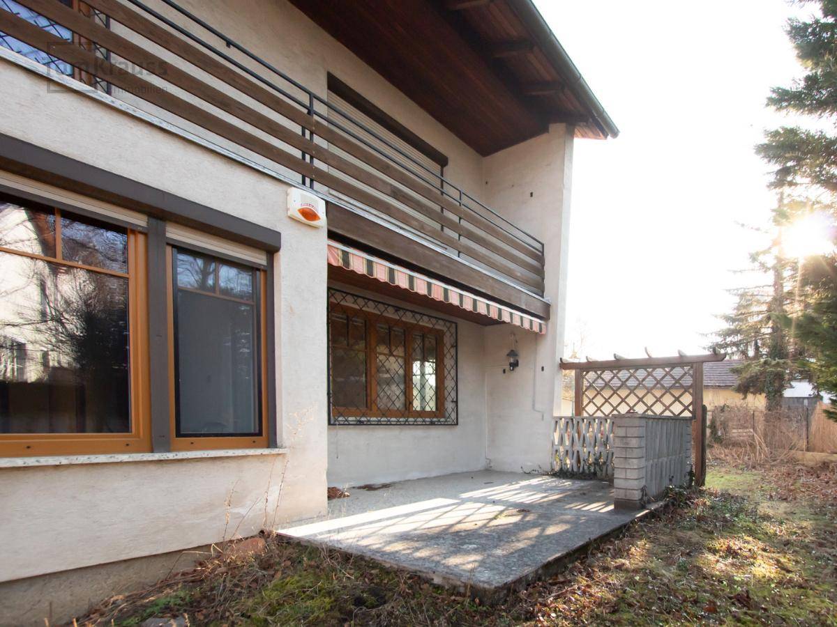 Betonierte Terrasse neben dem Haus mit Holzspalier und Blick auf den Gartenbereich.