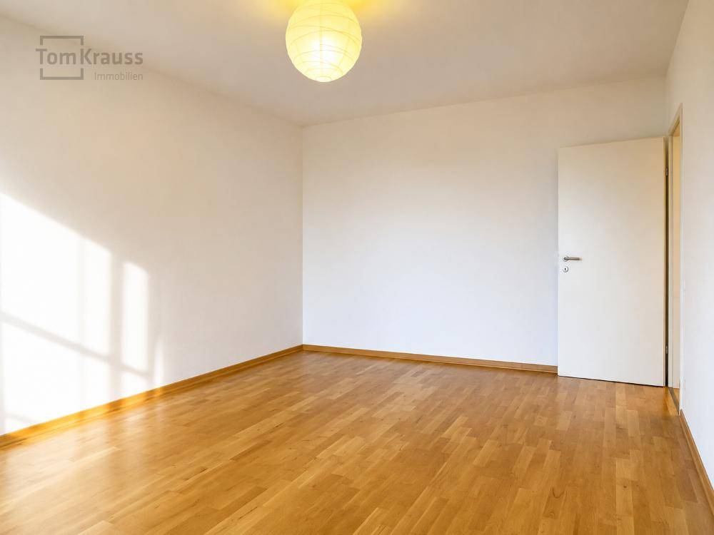 Helles, leeres Zimmer mit Holzboden und weiß gestrichenen Wänden, bereit zur Einrichtung.